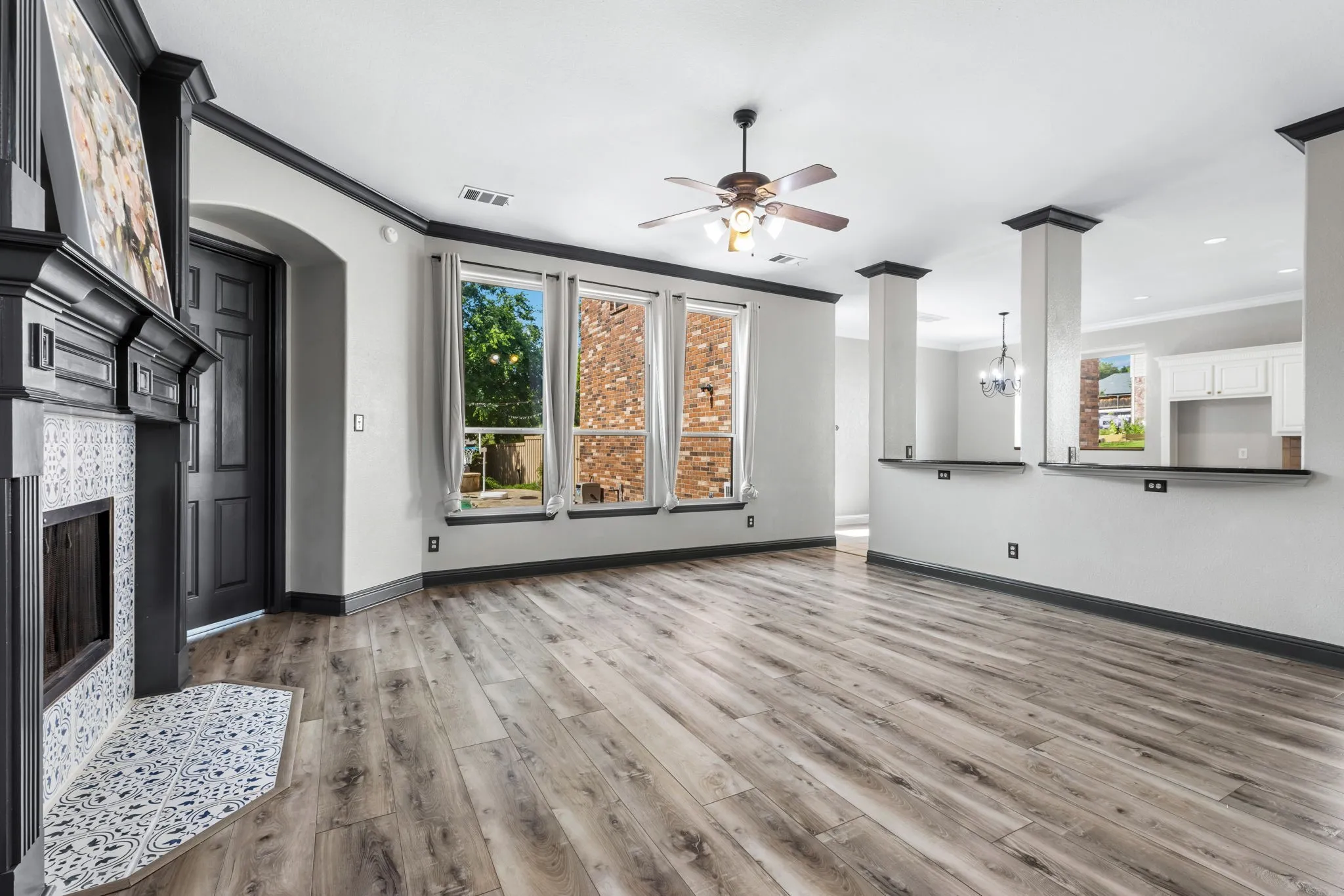 Spacious living area featuring wood-finish flooring, a decorative fireplace with patterned tile surround, multiple windows, a ceiling fan, and architectural half-walls