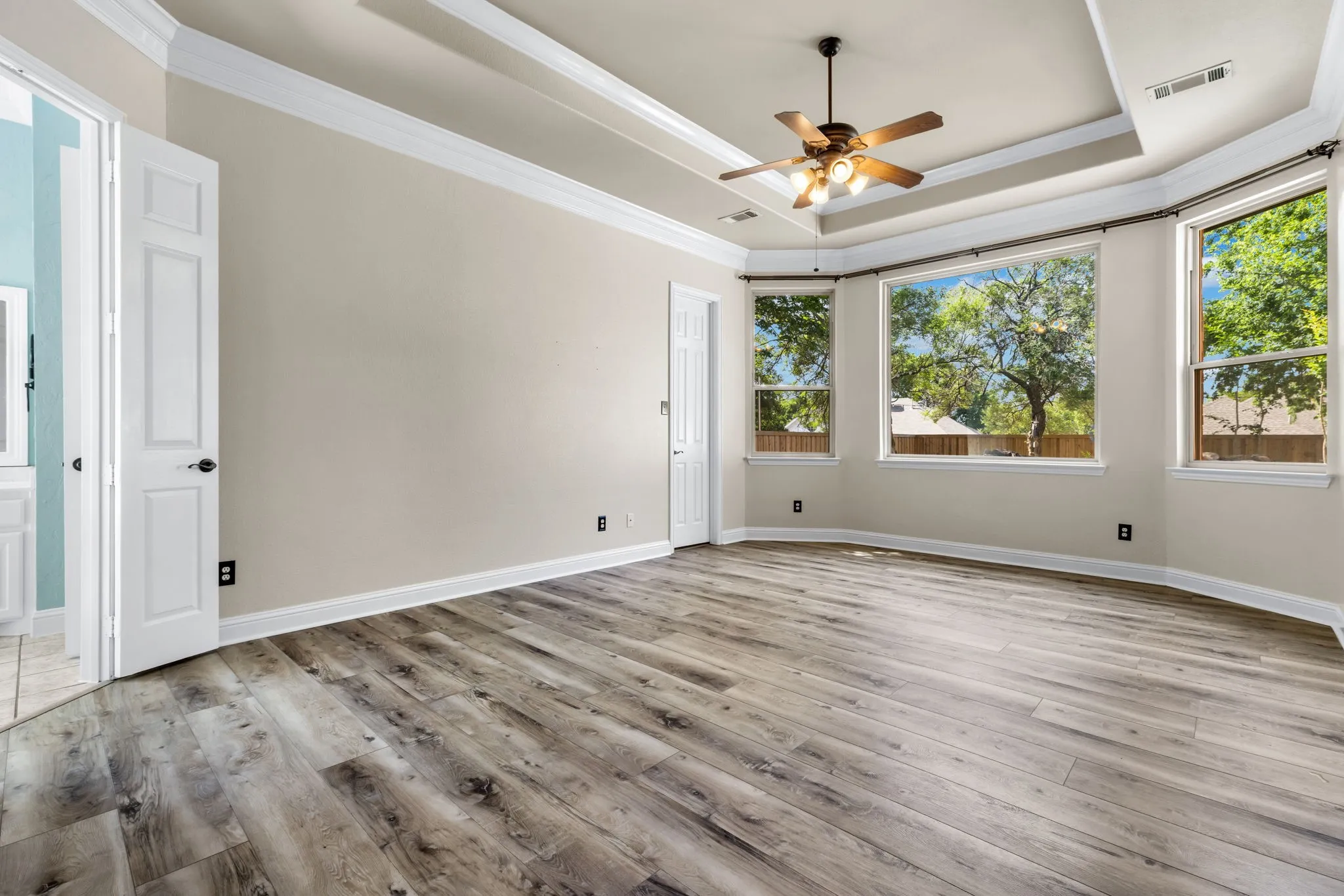 Spacious Primary bedroom featuring wood-finish flooring, a tray ceiling with crown molding, and 2 walk in closets