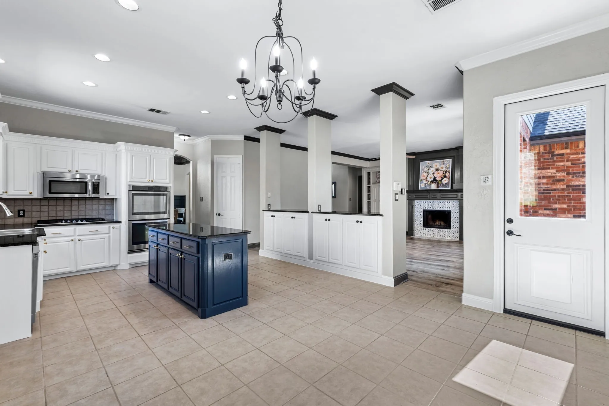 Spacious kitchen featuring a dark blue central island, white cabinetry, integrated stainless steel appliances, and tile flooring