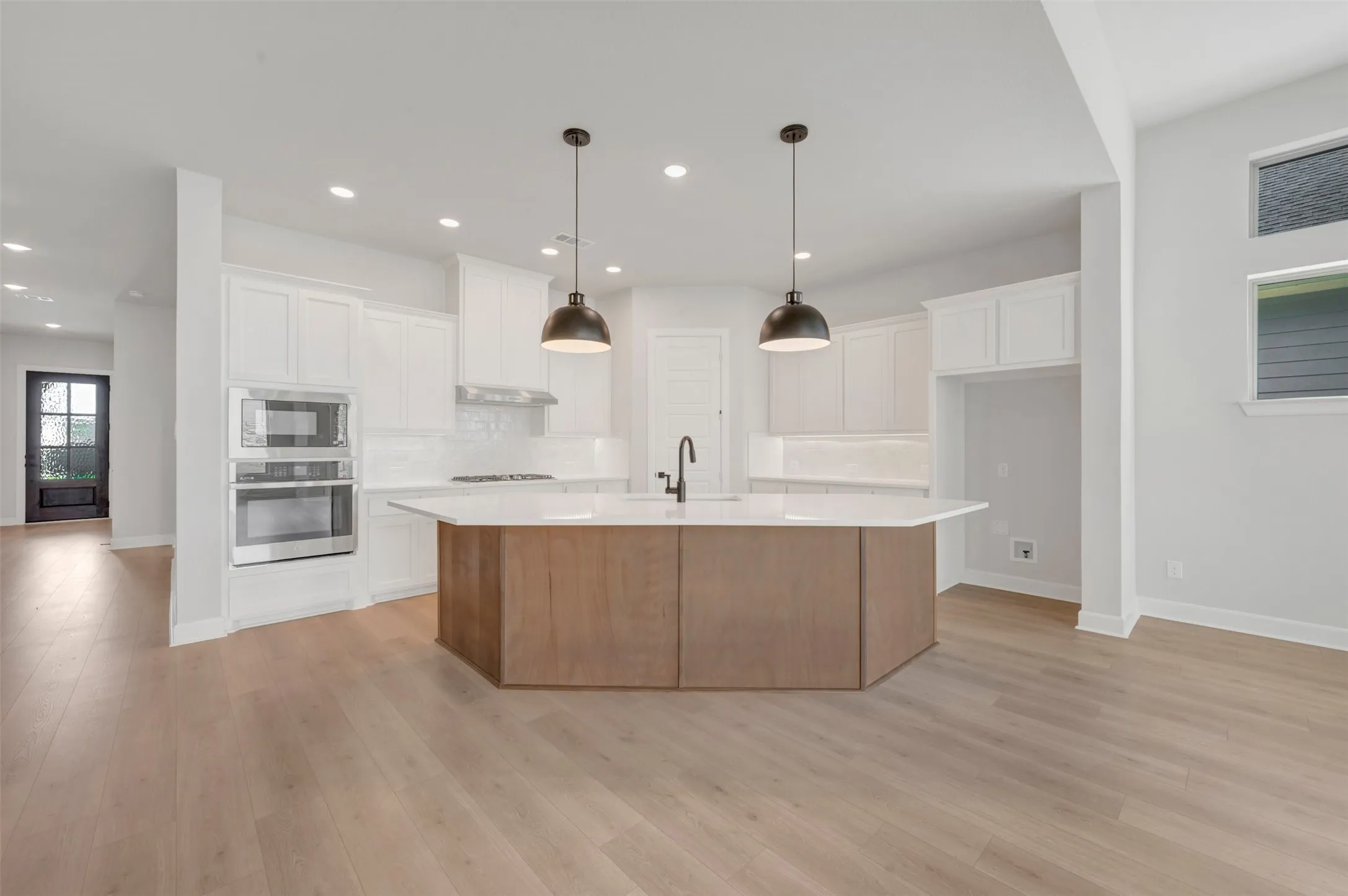 Open-concept kitchen featuring a multi-sided island with wood-finish paneling, white shaker cabinetry, stainless steel double ovens, and recessed lighting