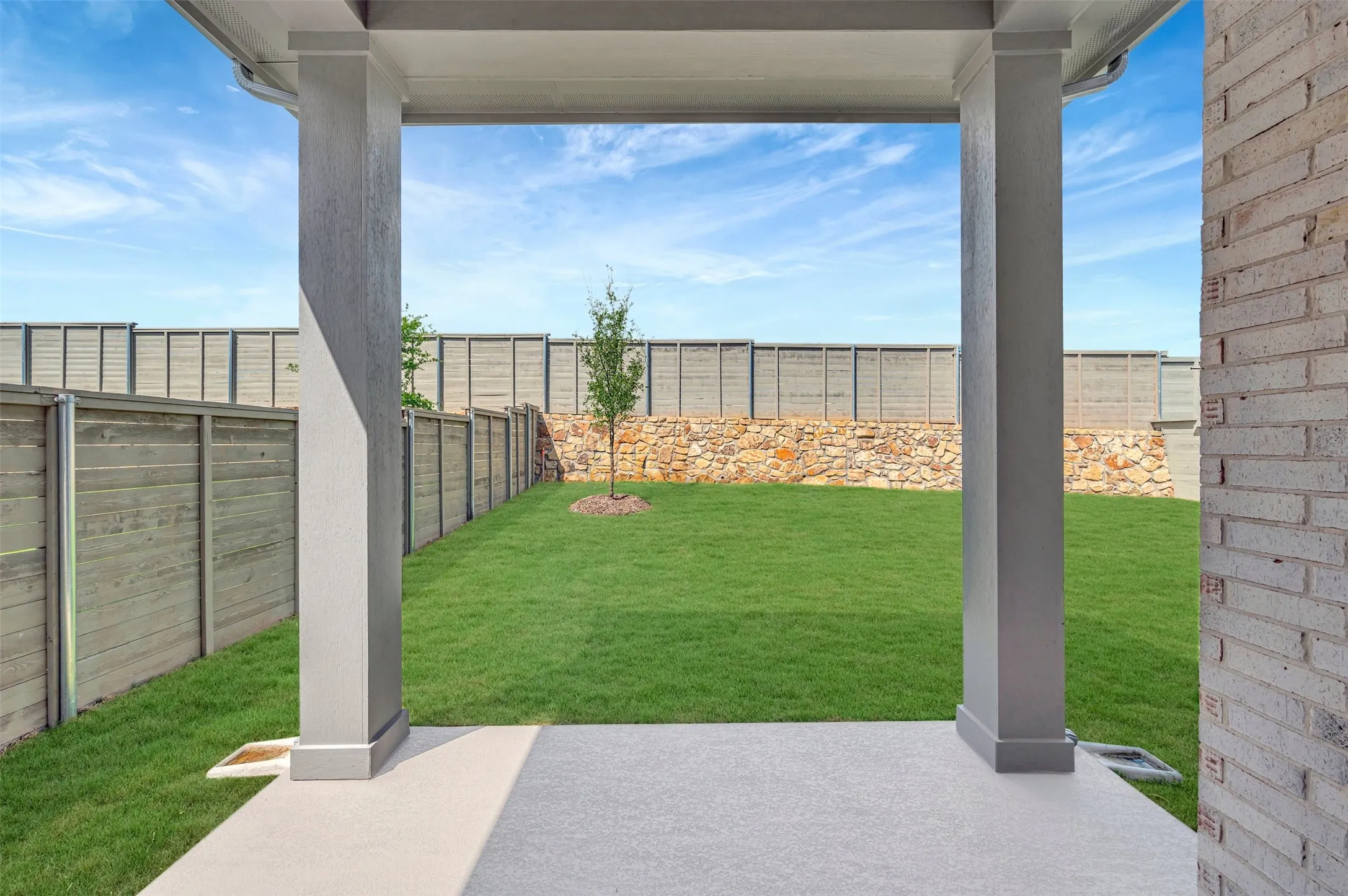 Covered patio with a concrete surface, featuring a spacious lawn and a young tree