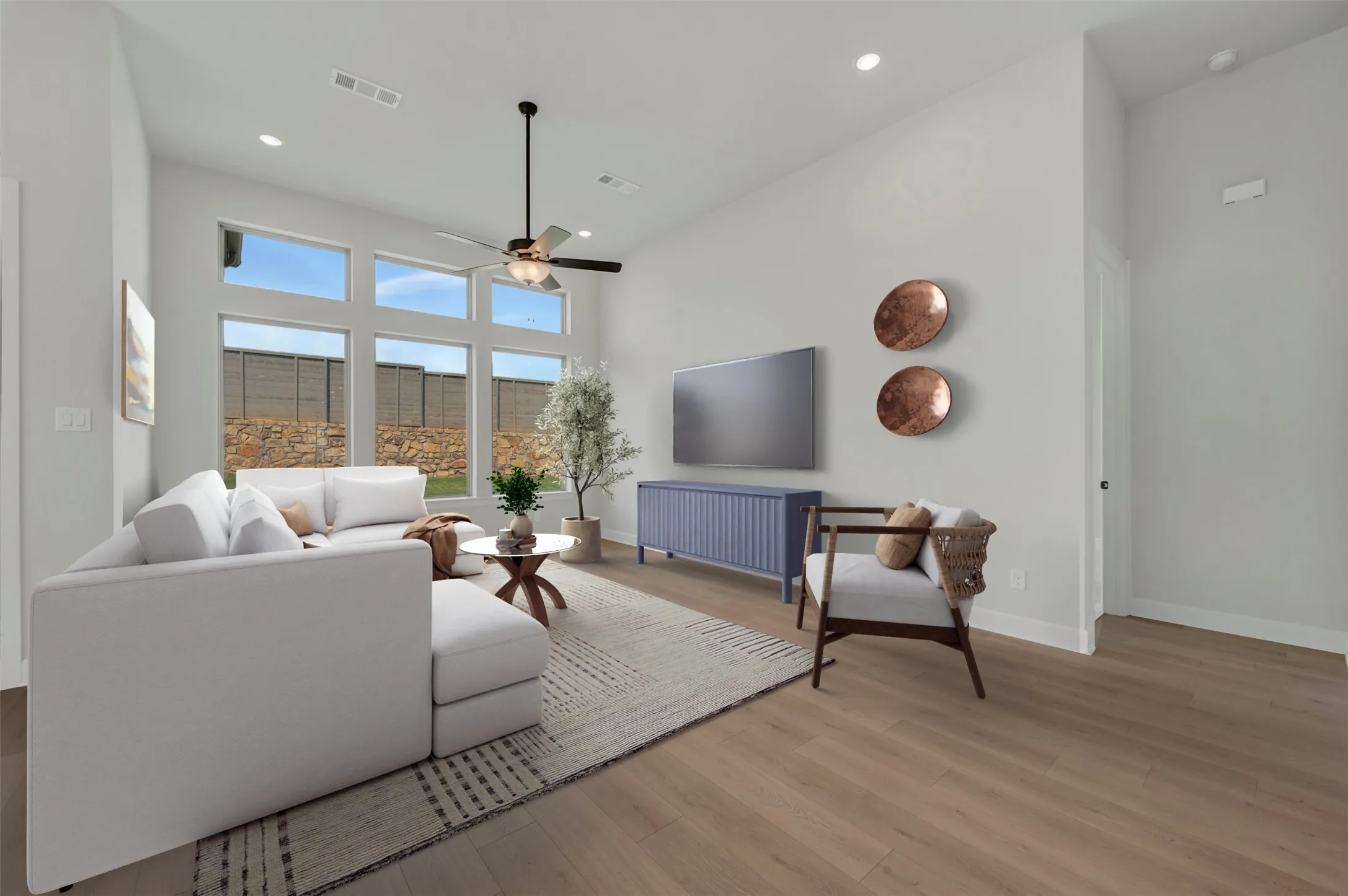 Living area featuring high ceilings, wood-finish flooring, a contemporary ceiling fan, recessed lighting, and a large window wall overlooking a privacy fence