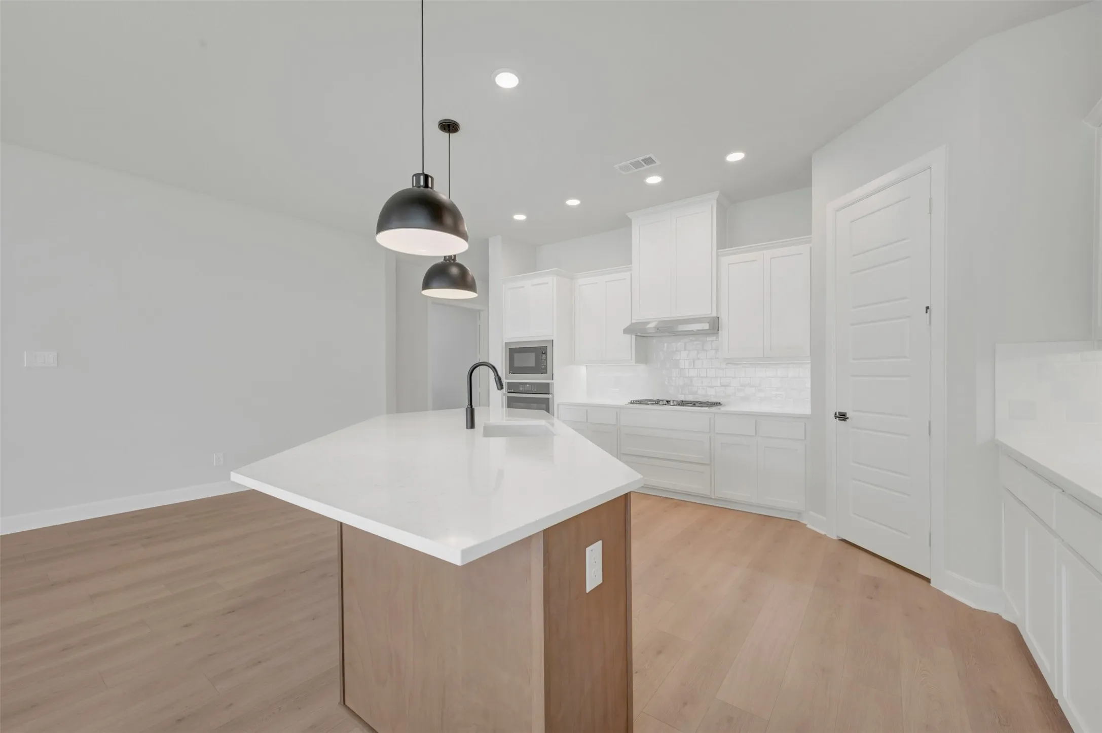 Modern kitchen featuring a central island with a waterfall-edge white countertop and a matte black faucet