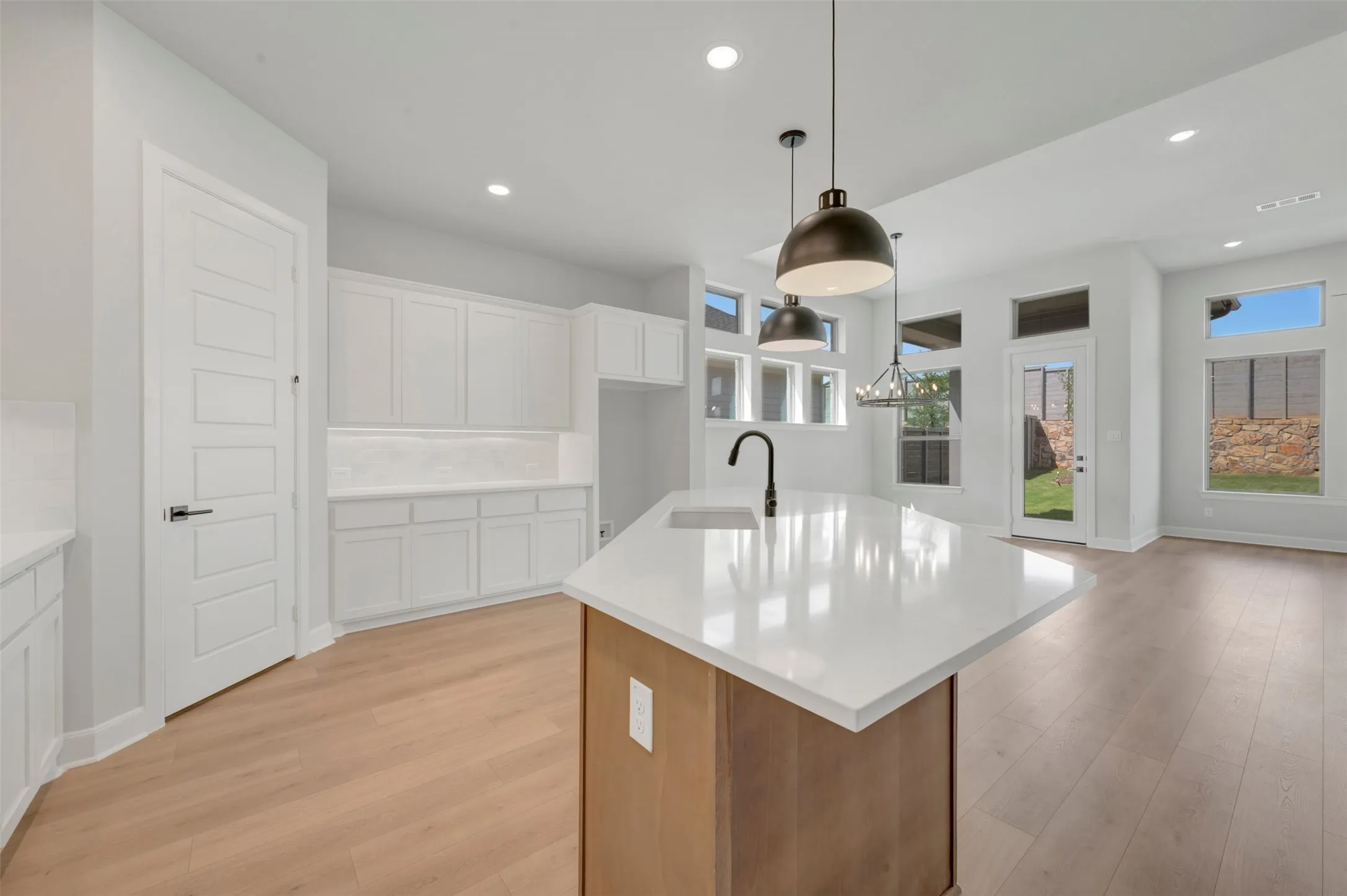 Open-concept kitchen featuring a large central island with a white countertop and integrated sink, pendant lighting, white cabinetry, and wood-finish flooring