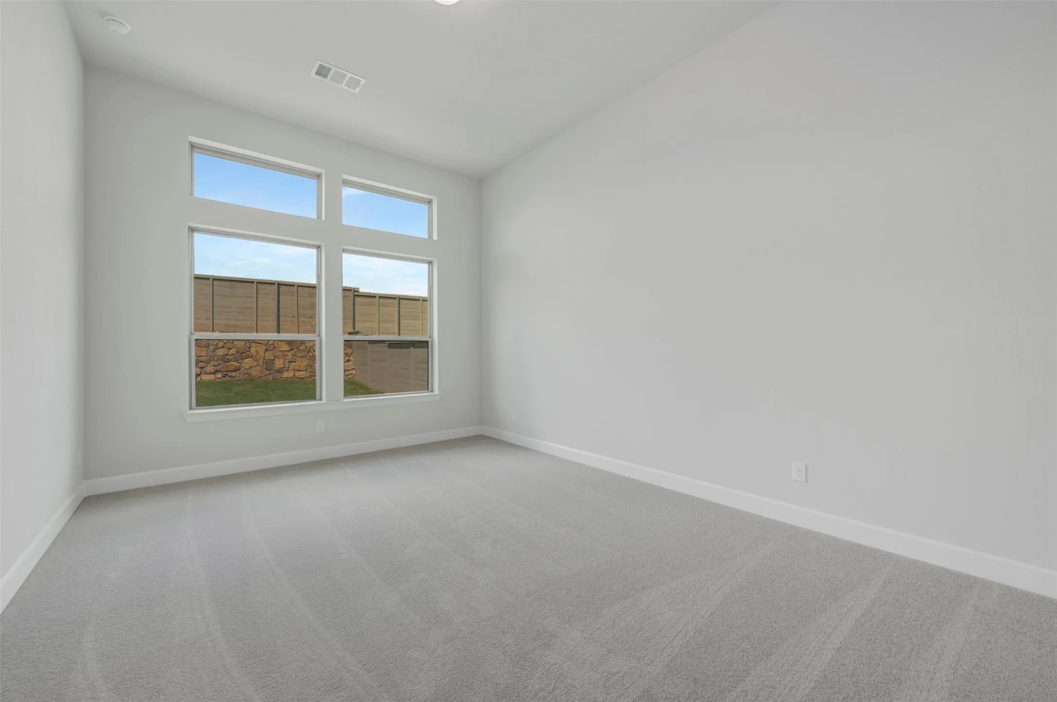 Spacious room featuring multiple transom windows, light gray wall paint, white baseboards, and soft gray carpeting