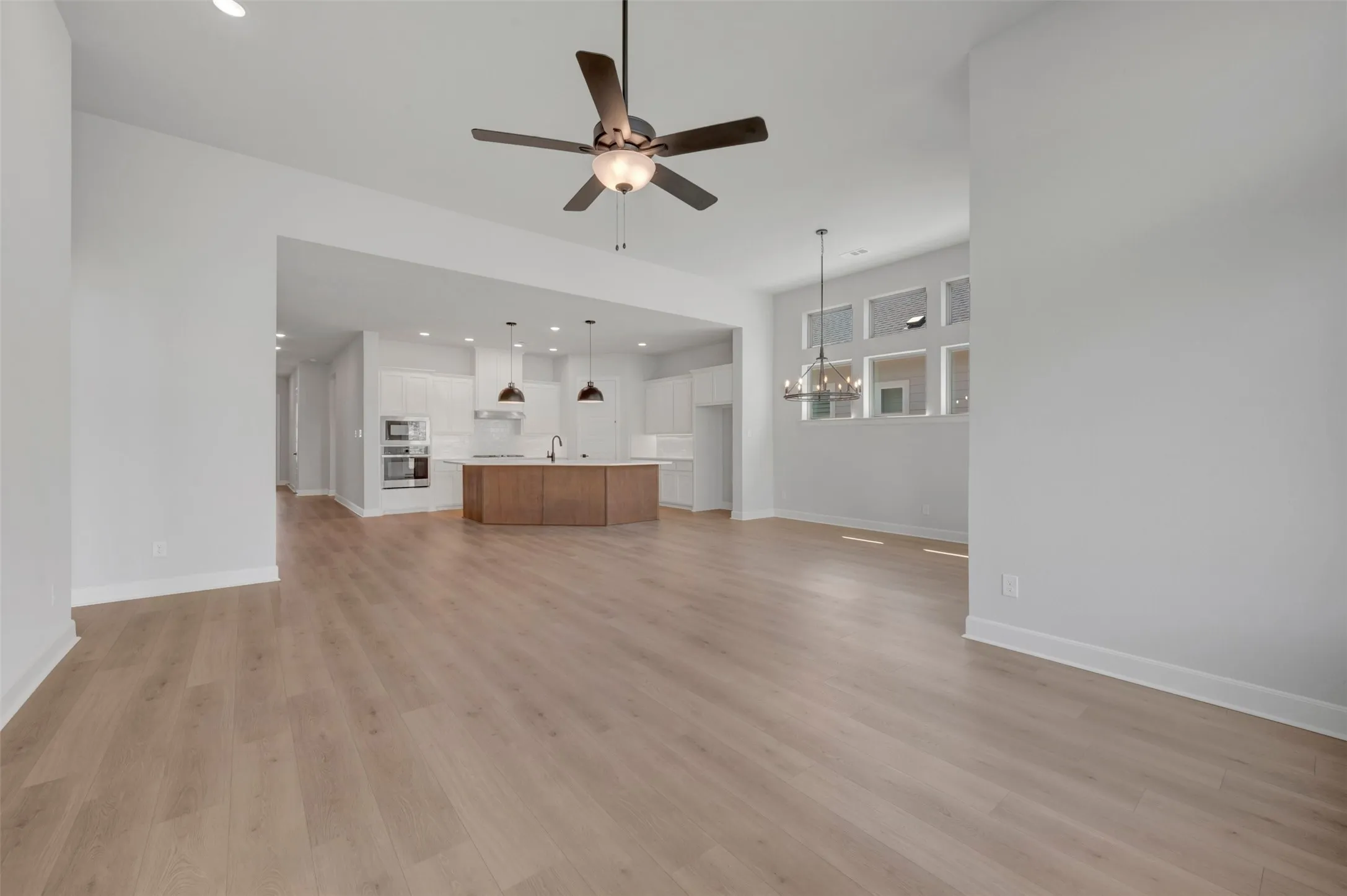Expansive open-concept living area featuring wood-finish flooring, a ceiling fan, recessed lighting, and a modern chandelier