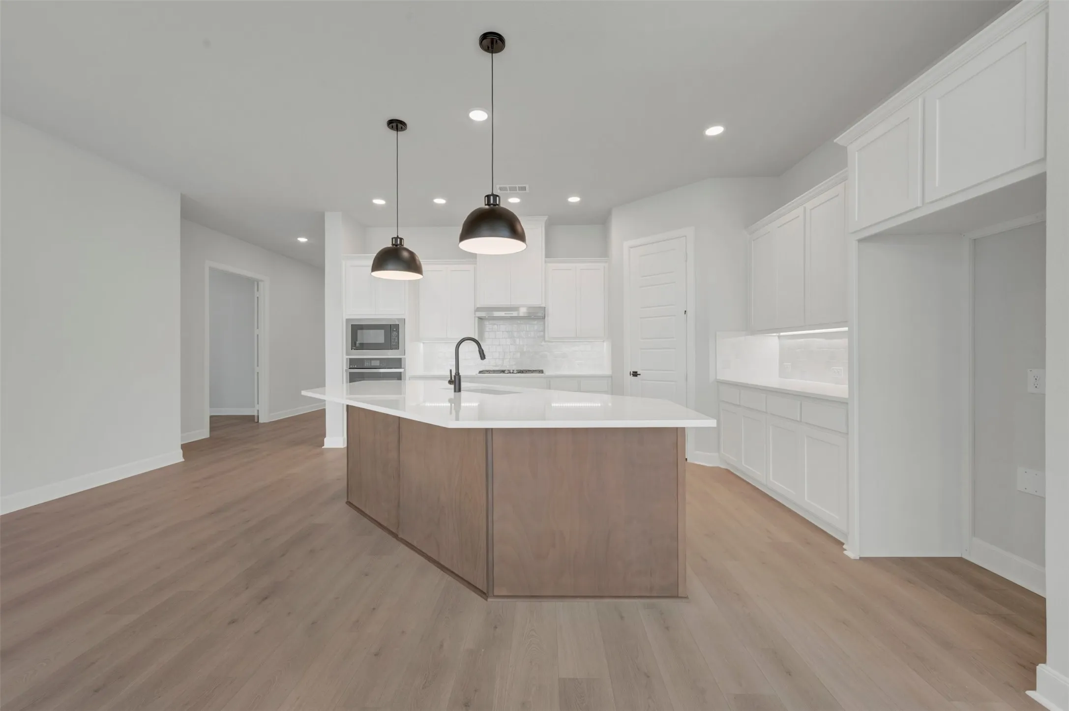 Kitchen featuring a large central island with a wood-finish base, white countertop, and integrated sink