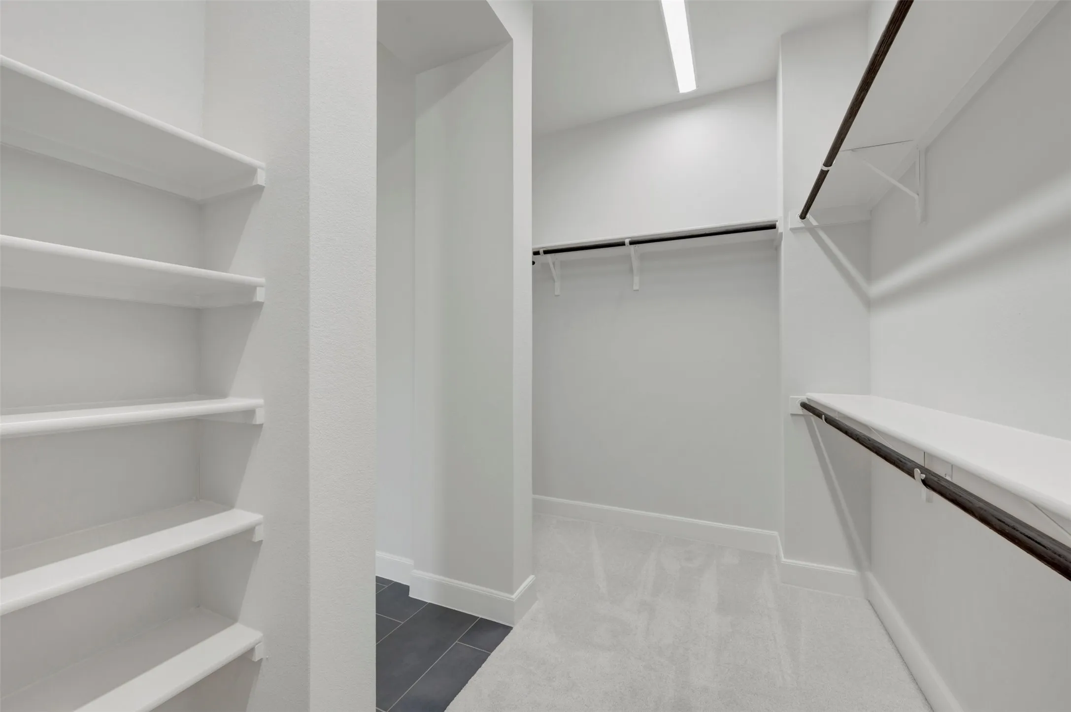 Spacious walk-in closet featuring extensive built-in shelving, multiple clothing rods, recessed lighting, and a combination of soft carpet and dark tile flooring