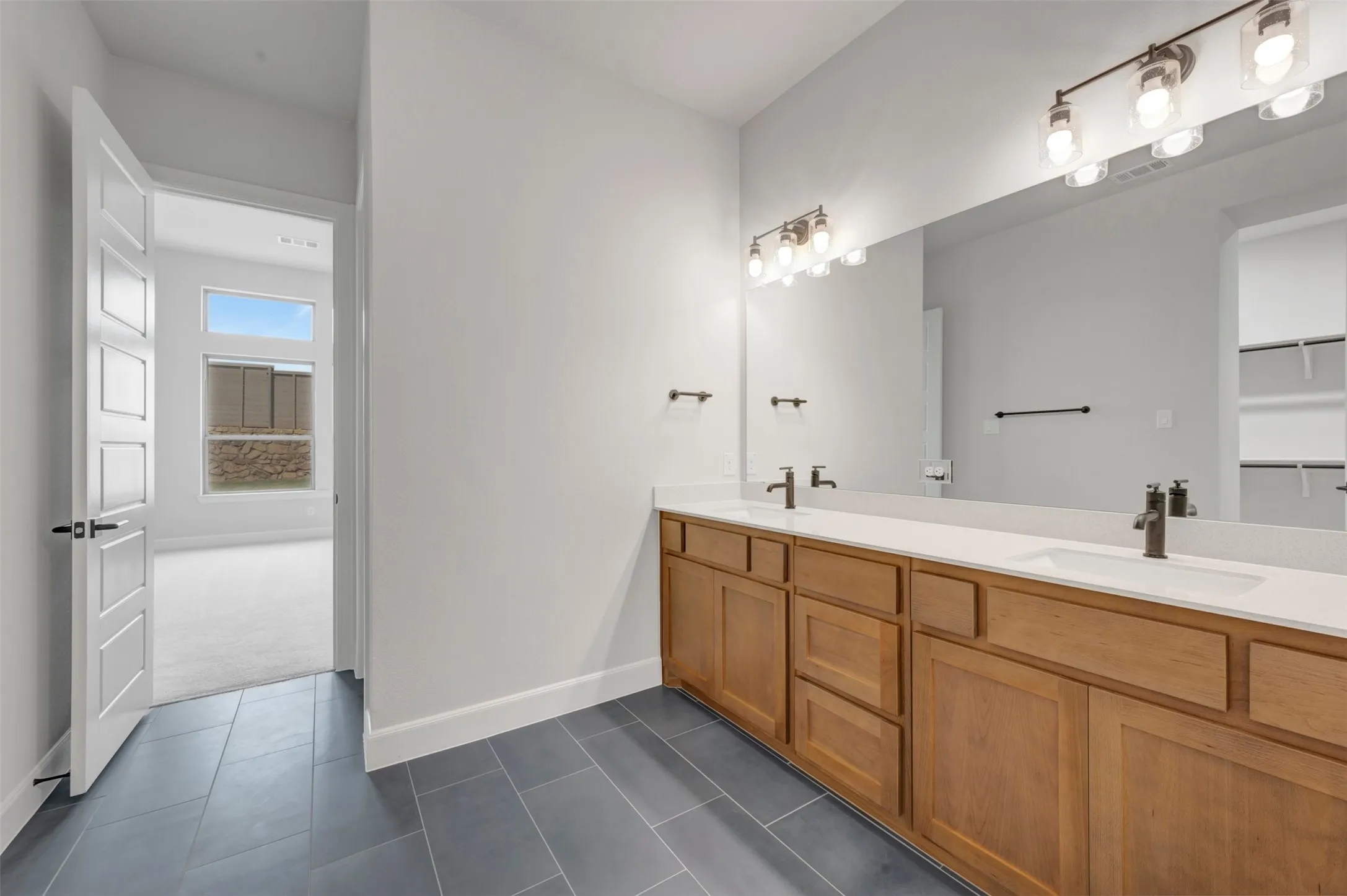 Double vanity bathroom featuring a light wood-finish cabinet, dual white undermount sinks, and a quartz countertop