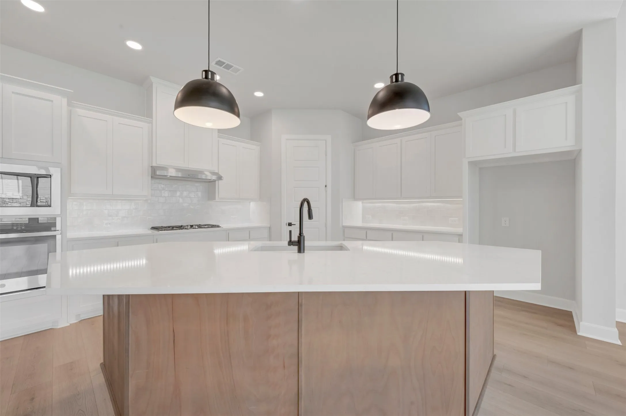 Expansive kitchen island with a light-toned countertop and wood-finish paneling, complemented by two contemporary pendant lights