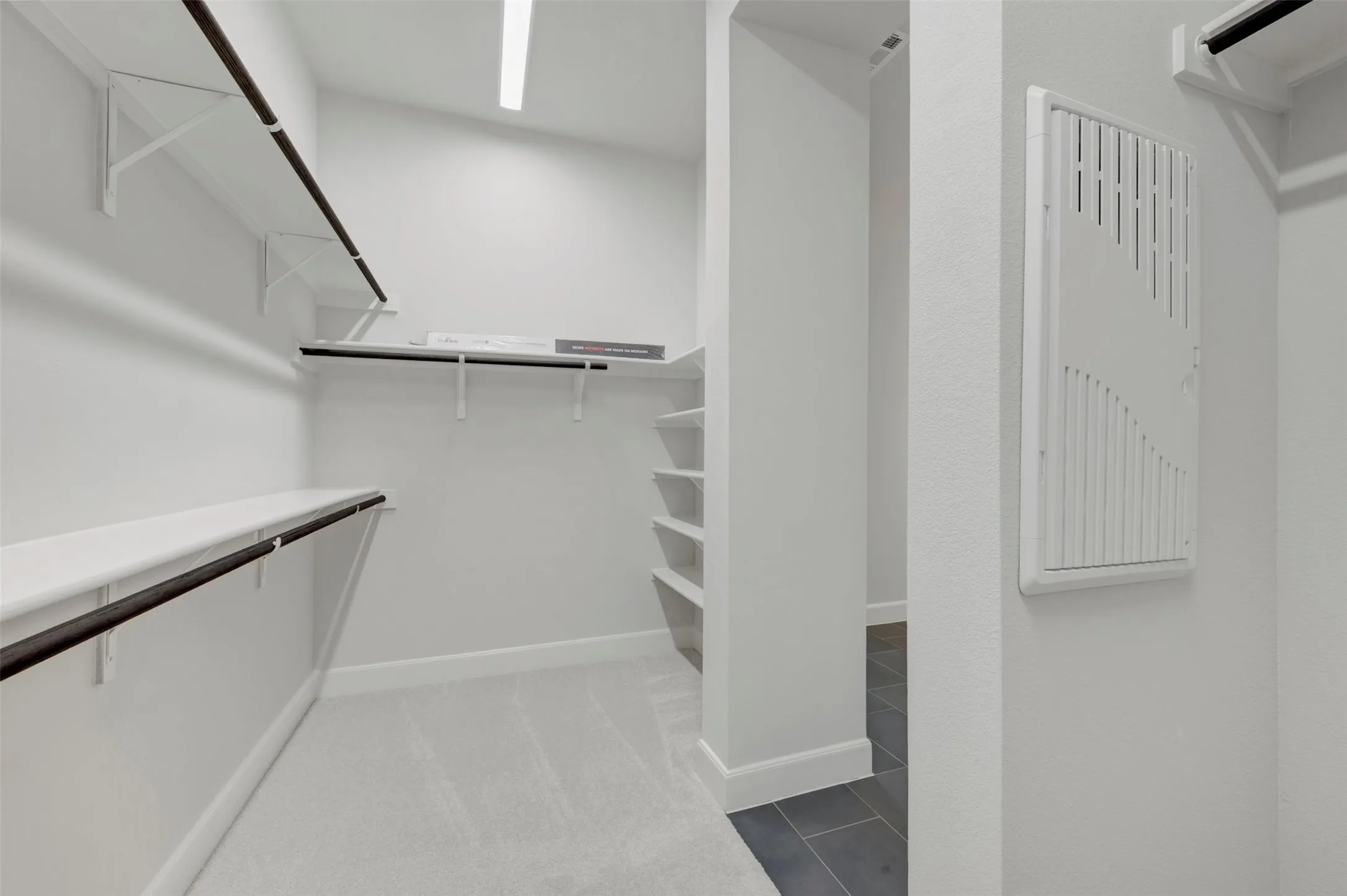 Spacious walk-in closet featuring light gray carpeting, multiple white shelving units, and dark-finish hanging rods