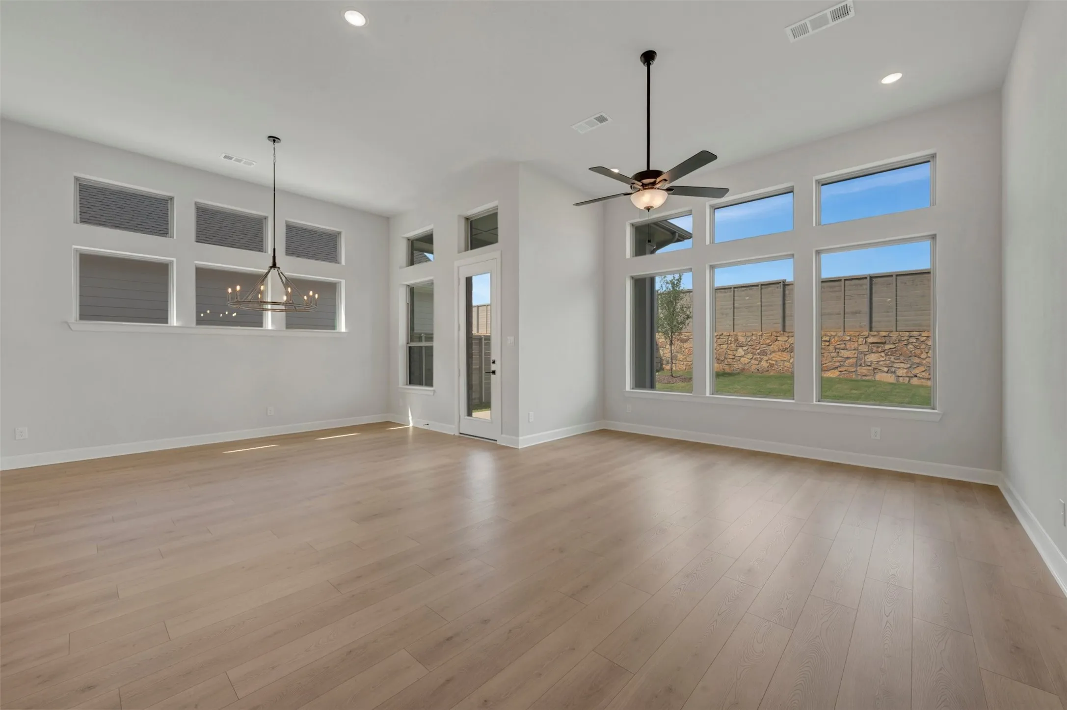 Expansive living area featuring light wood-finish flooring, high ceilings with recessed lighting, and a modern ceiling fan