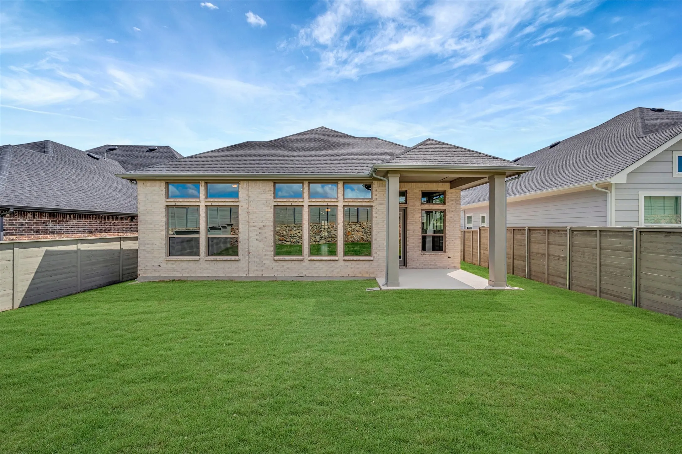 Expansive green lawn with a covered patio, light brick exterior, and a dark shingle roof