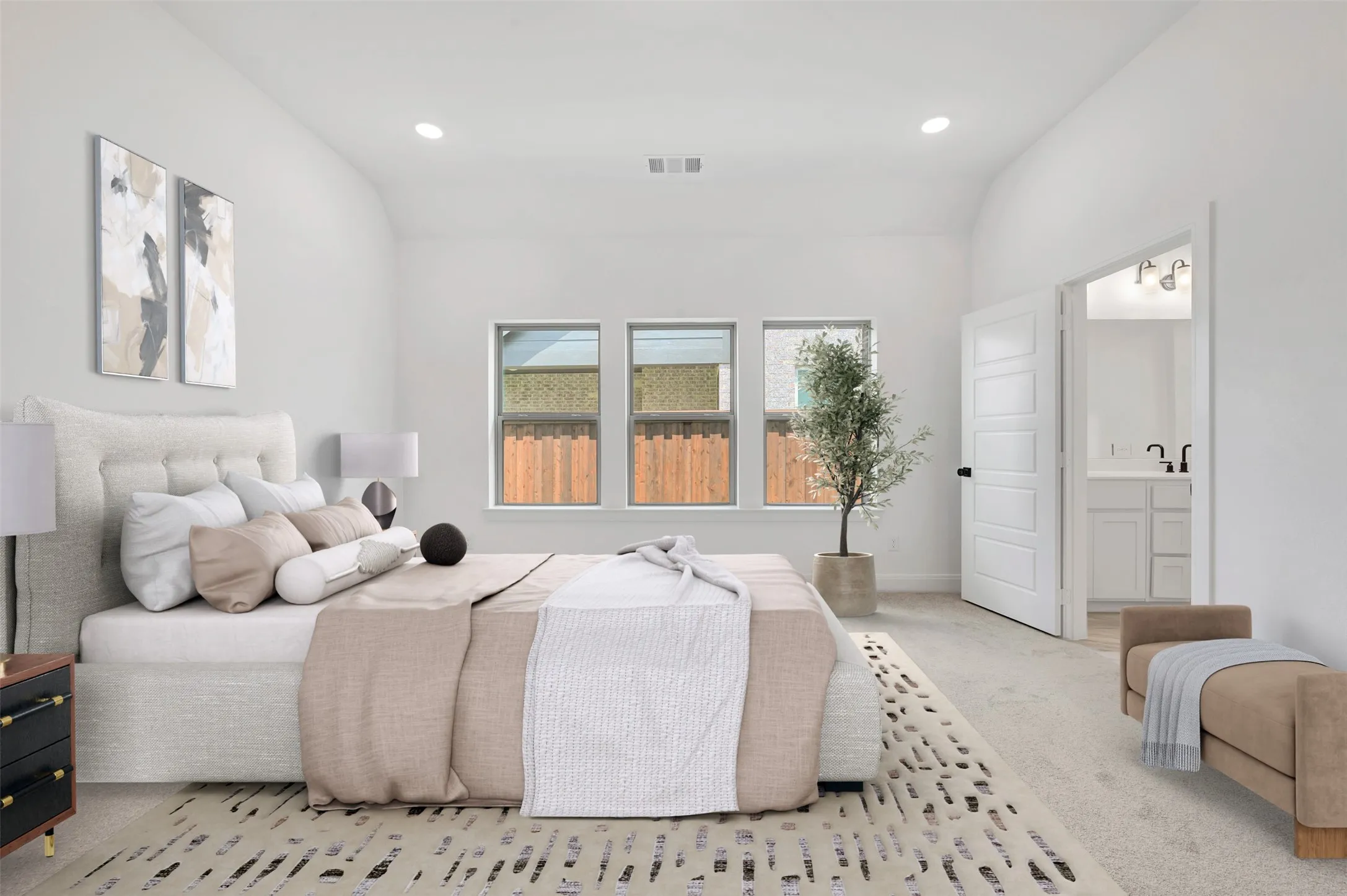 Spacious room featuring vaulted ceilings, recessed lighting, three large windows, light neutral carpet, and a door revealing a bathroom with a dual vanity