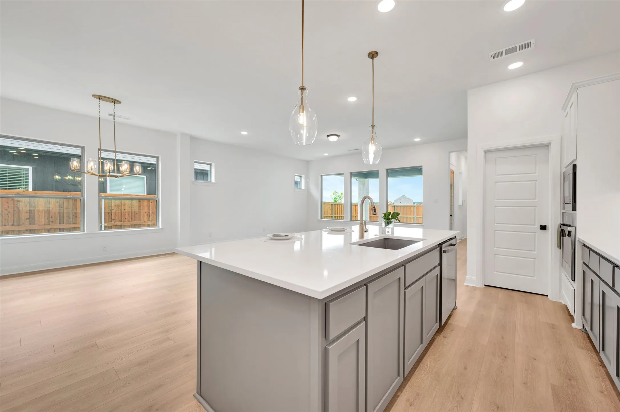 Open-concept living space featuring a kitchen island with a built-in sink, pendant lighting, wood-finish flooring, recessed lighting, and large windows