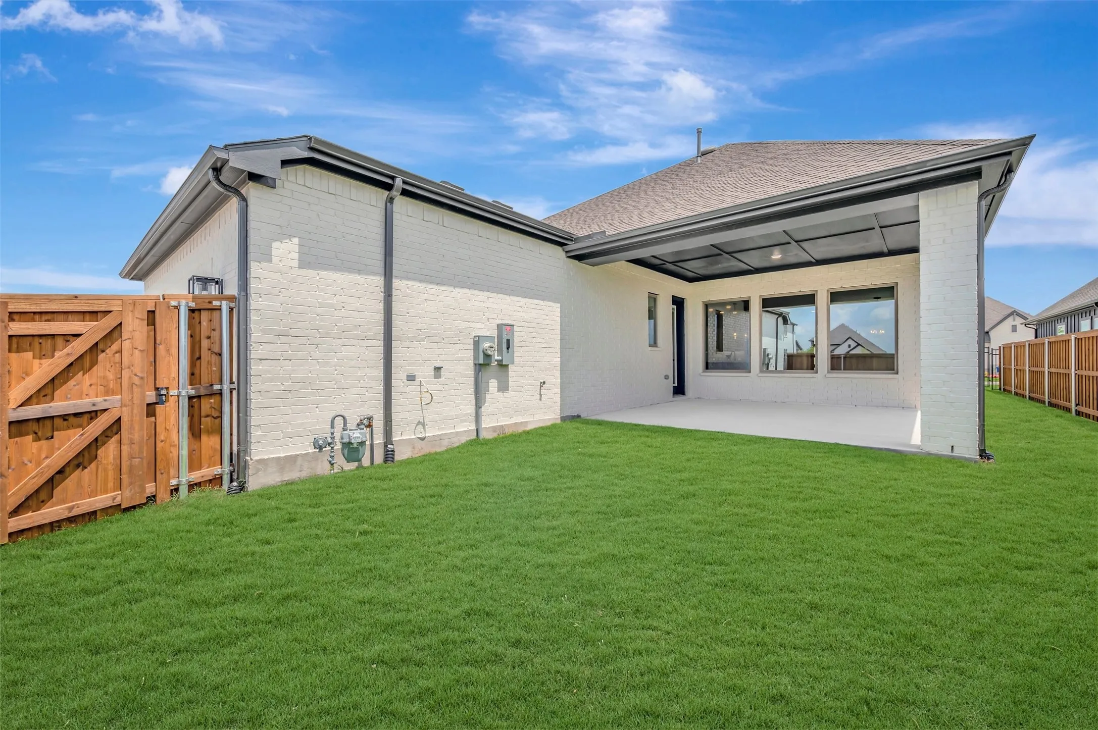Expansive green lawn with a covered patio, featuring large windows and a privacy fence