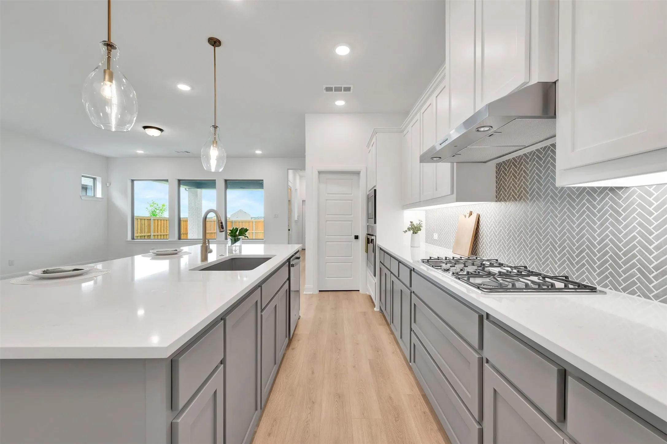 Open-concept kitchen featuring an expansive island with a built-in sink, white countertops, and wood-finish flooring