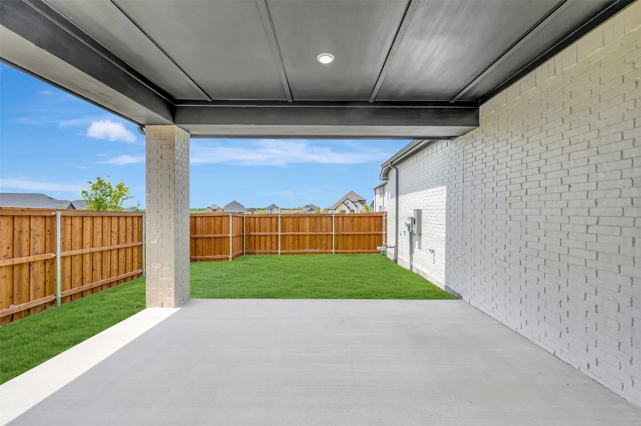 Covered concrete patio featuring a white painted brick exterior wall and a dark gray paneled ceiling with recessed lighting