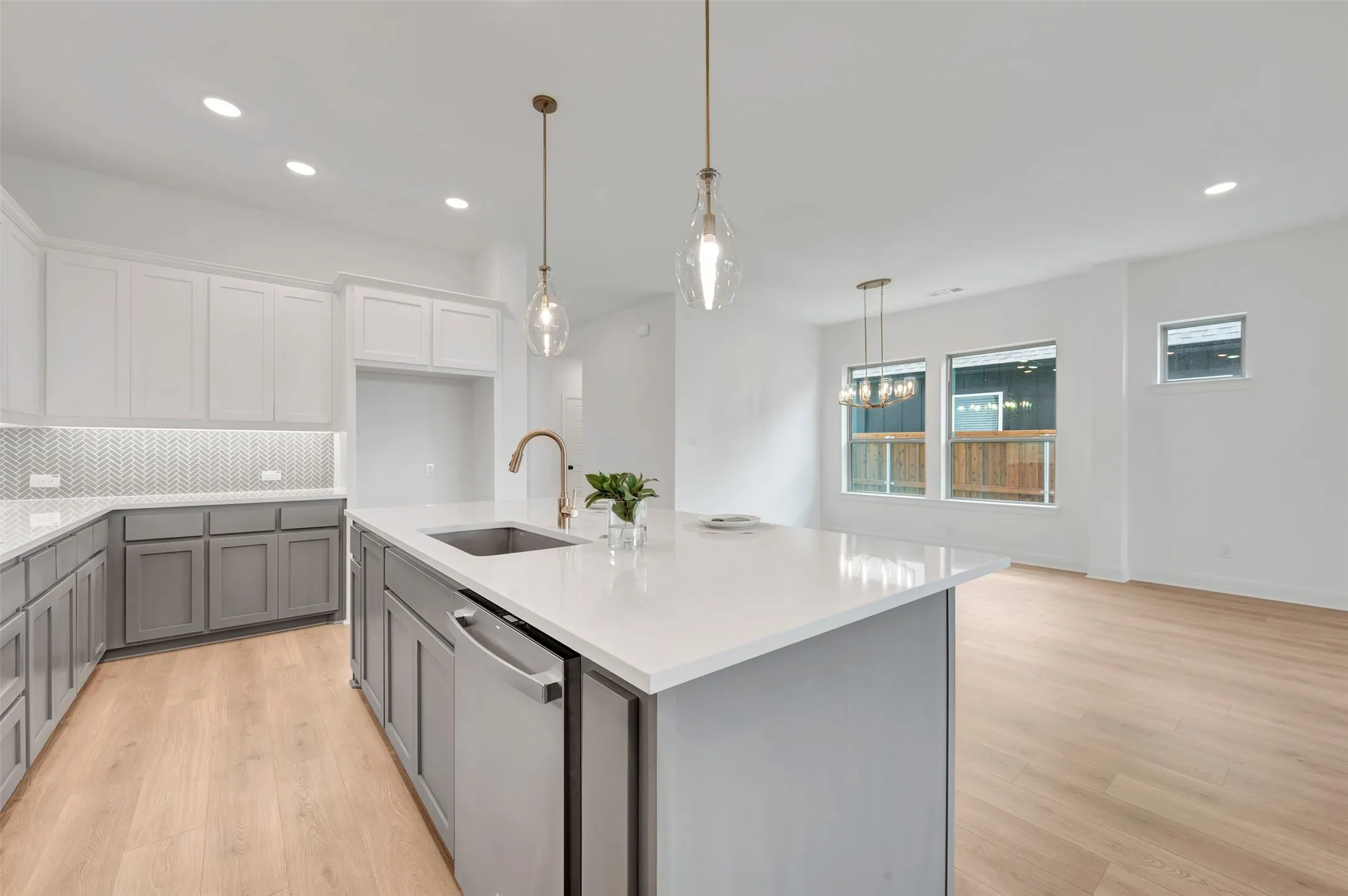Contemporary kitchen featuring an expansive island with a stainless steel dishwasher, white countertops, and a brass-finish faucet