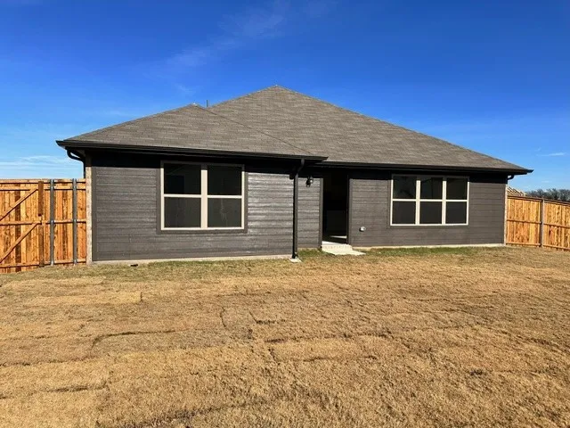 Rear view of house with a fenced backyard and roof with shingles