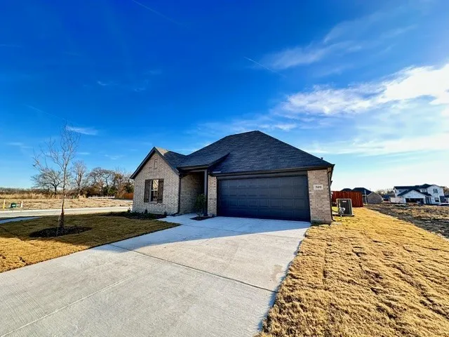 View of front of home with concrete driveway, brick siding, a garage, and a front lawn