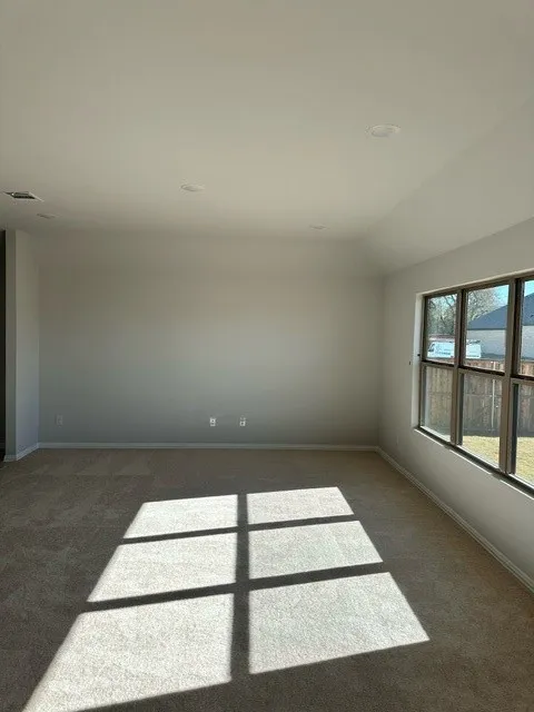 Empty room with dark colored carpet and lofted ceiling