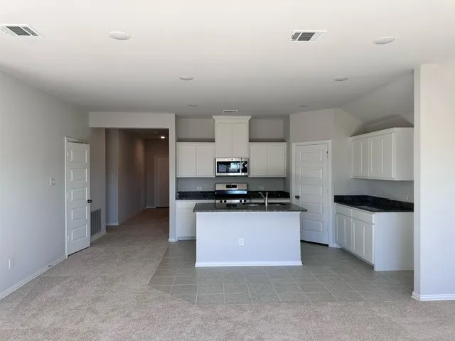 Kitchen with white cabinets, light carpet, stainless steel appliances, and a center island with sink