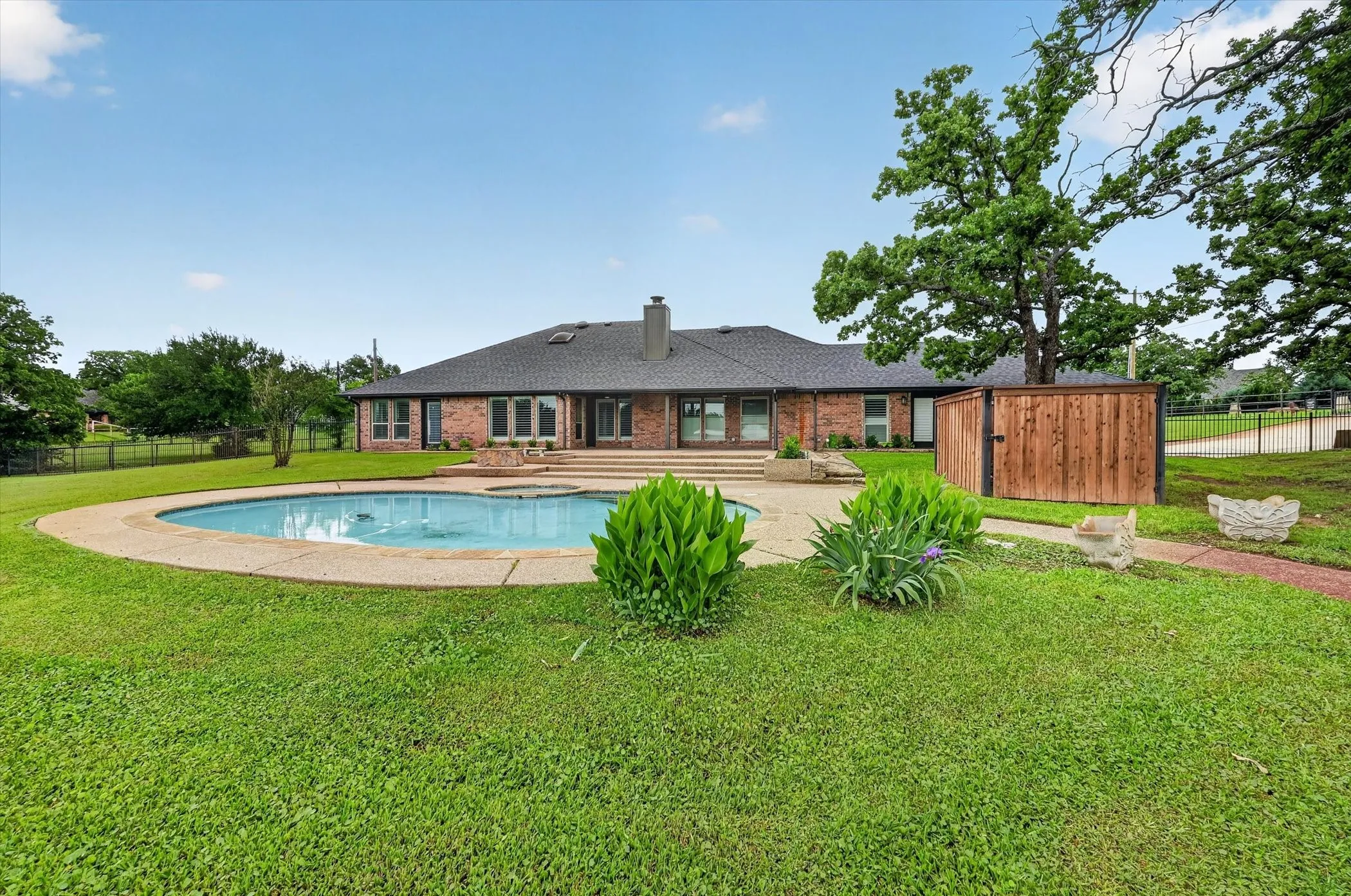 Spacious brick exterior featuring a large in-ground pool, integrated spa, and extensive concrete surround