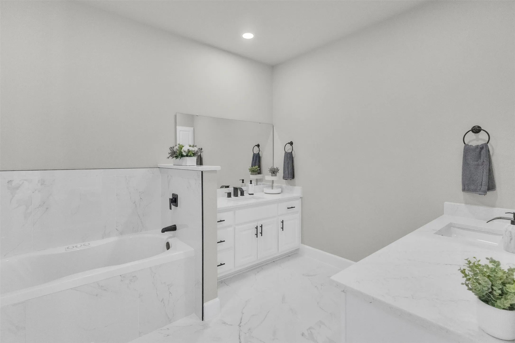 Full bathroom featuring a garden tub, two vanities, recessed lighting, and light marble finish floors