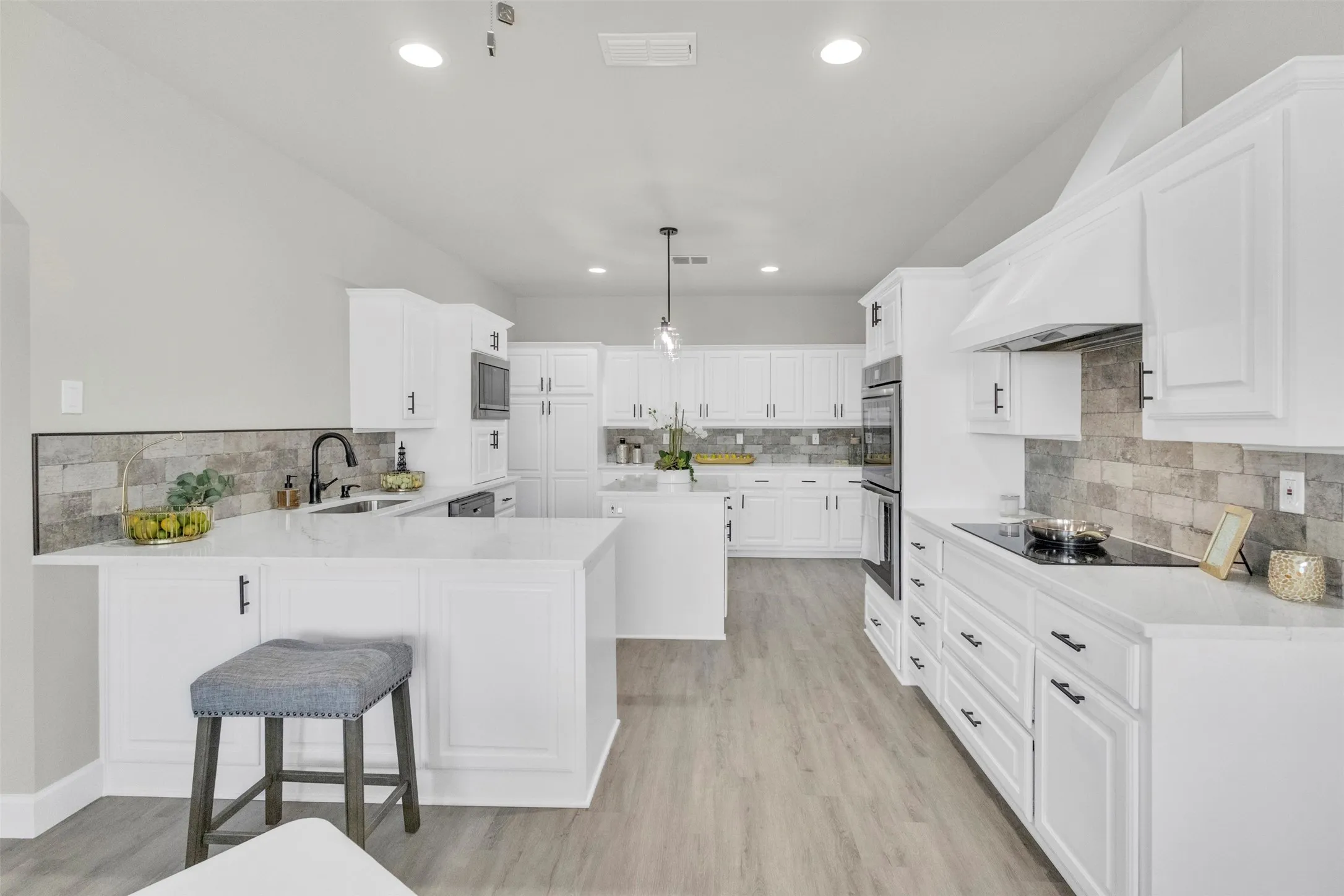 Kitchen featuring a peninsula, a breakfast bar, white cabinetry, a center island, and light stone counters