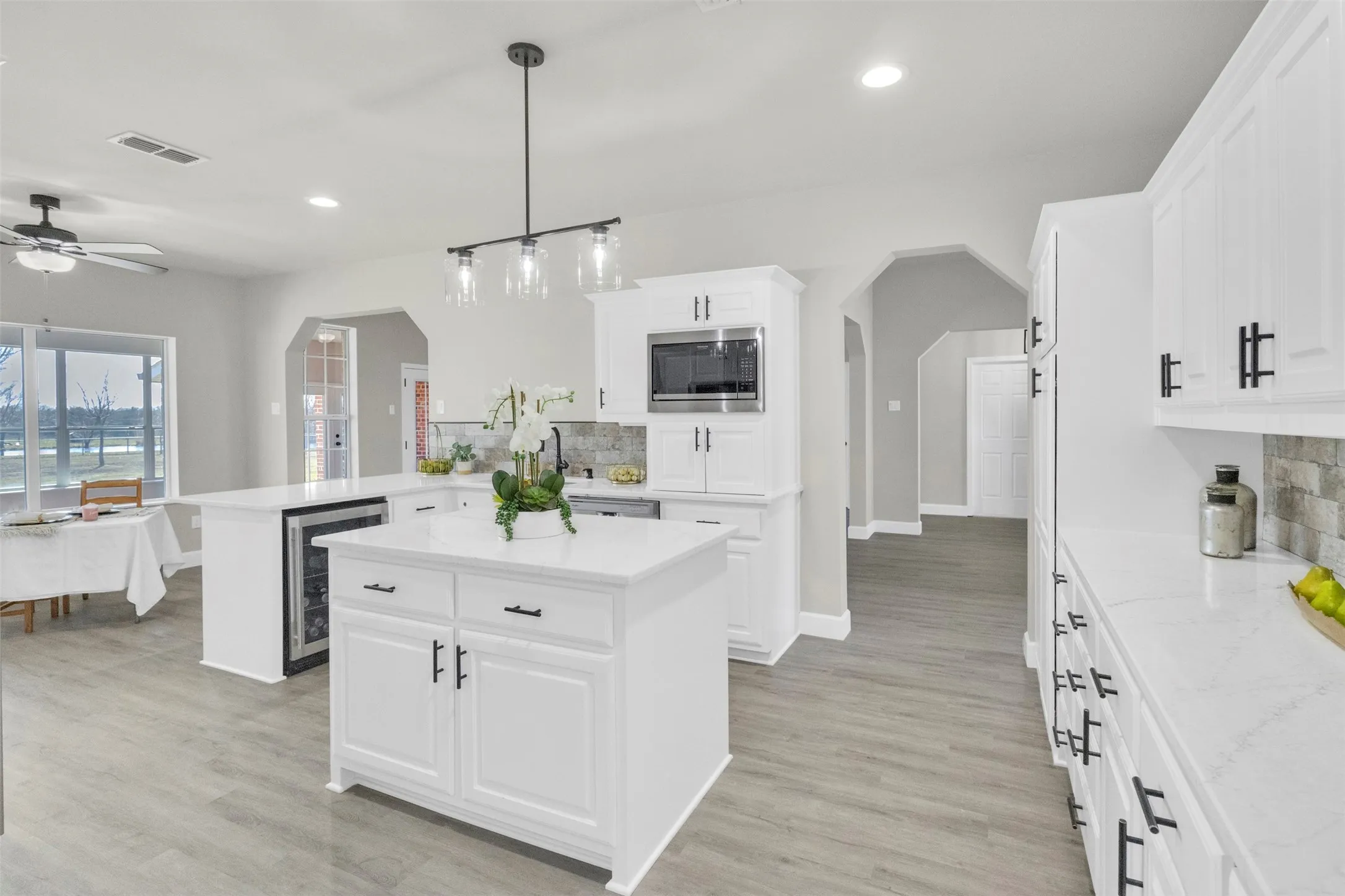 Kitchen with arched walkways, a peninsula, a center island, backsplash, and beverage cooler