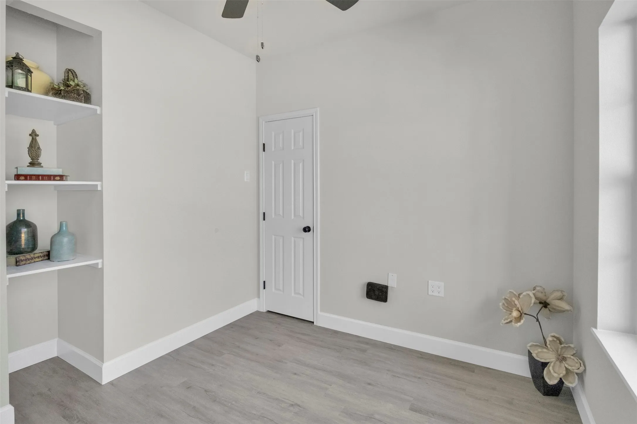 Empty room with ceiling fan, light wood finished floors, and built in features