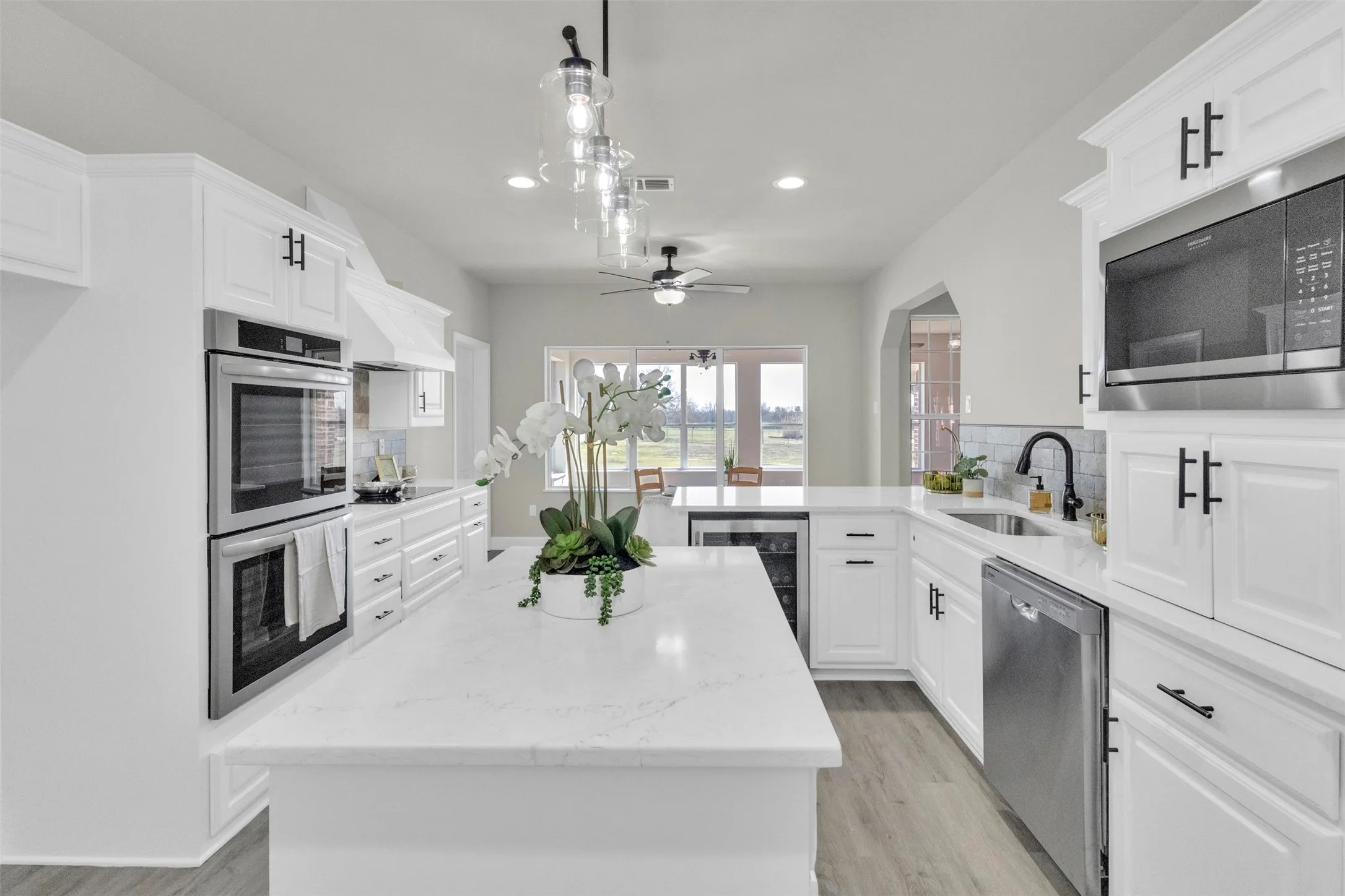 Kitchen with a peninsula, wine cooler, stainless steel appliances, white cabinetry, and a center island