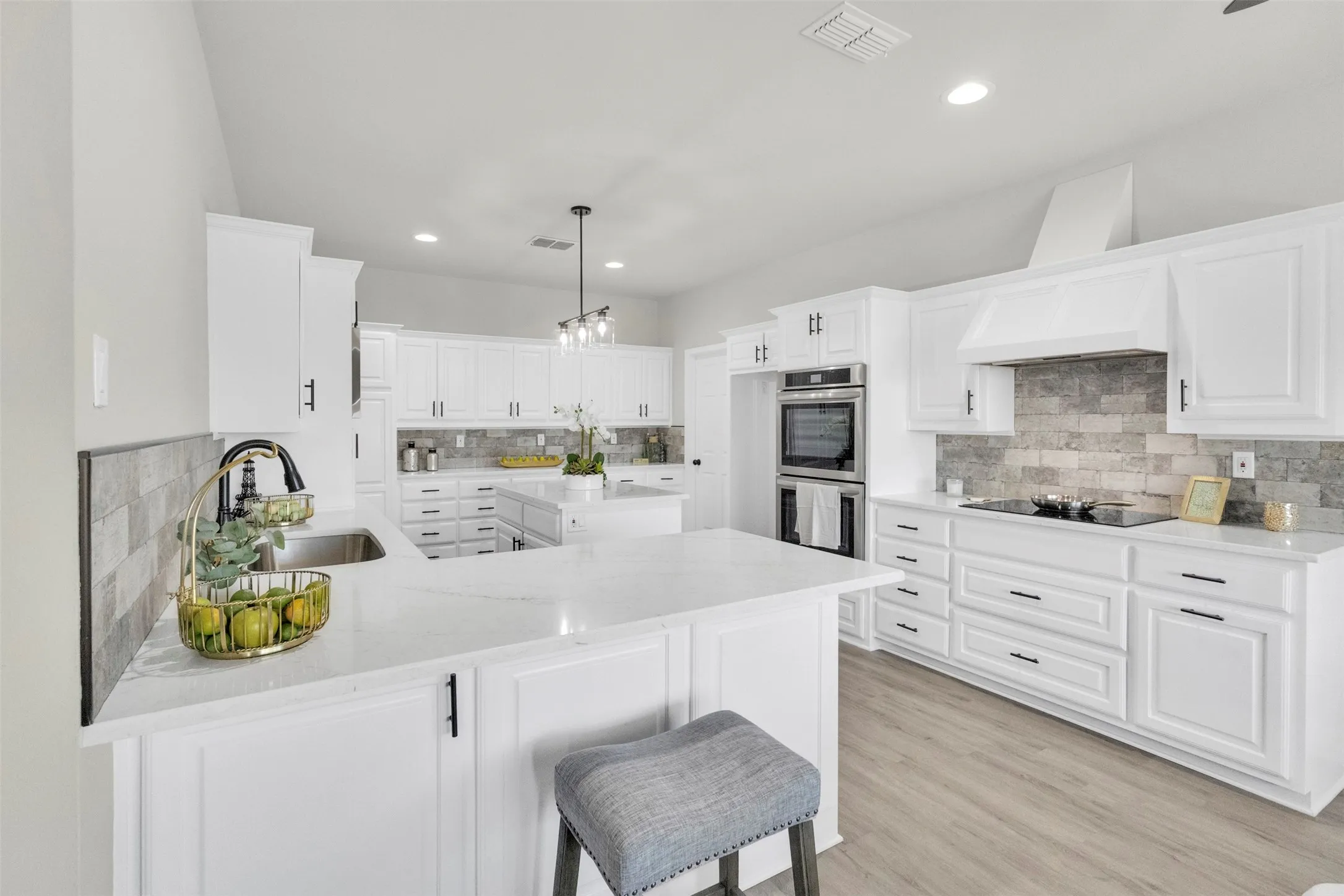 Kitchen with a peninsula, light stone counters, white cabinets, and decorative backsplash