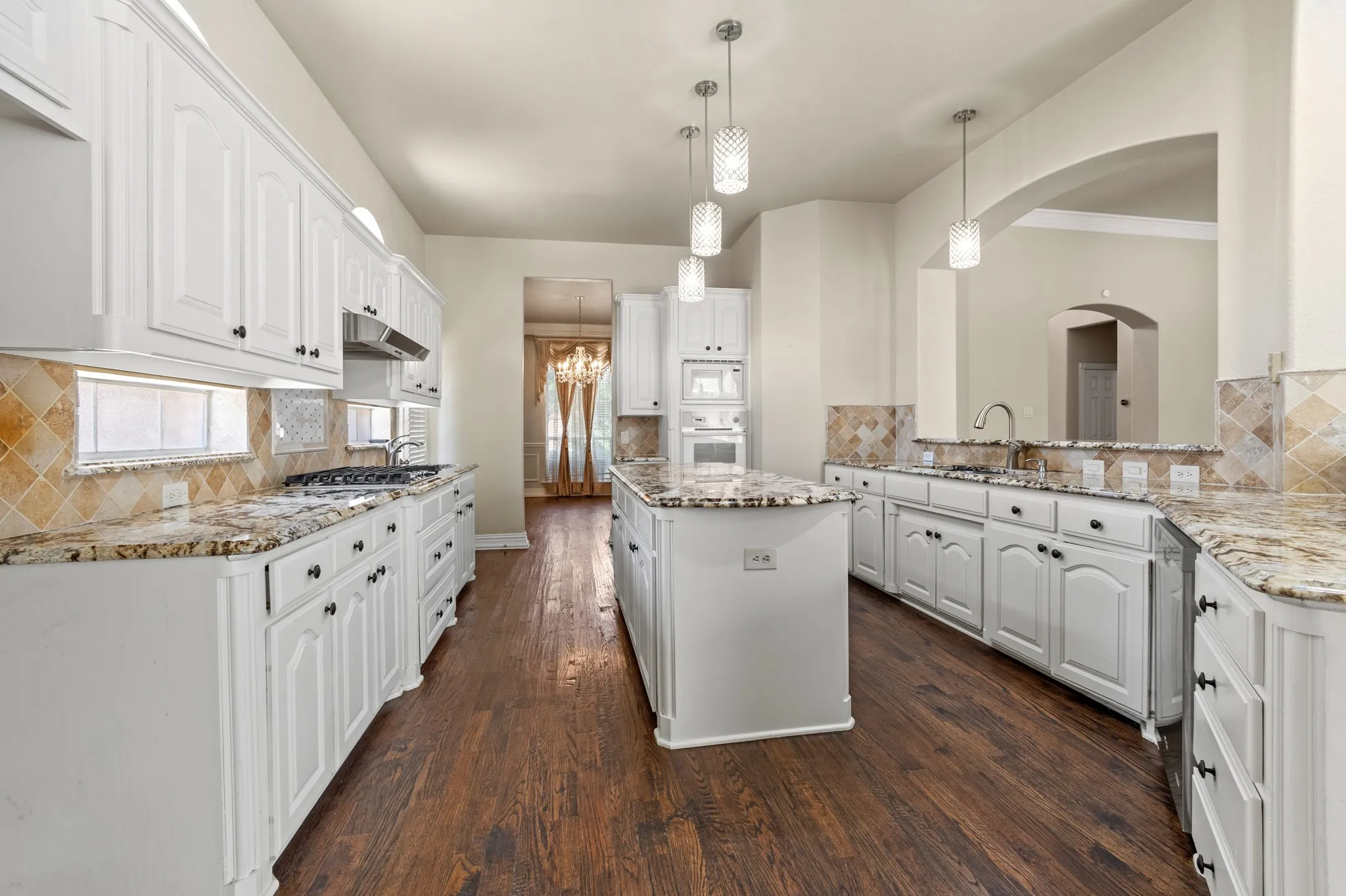 Kitchen with tasteful backsplash, white cabinetry, a center island, white appliances, and pendant lighting