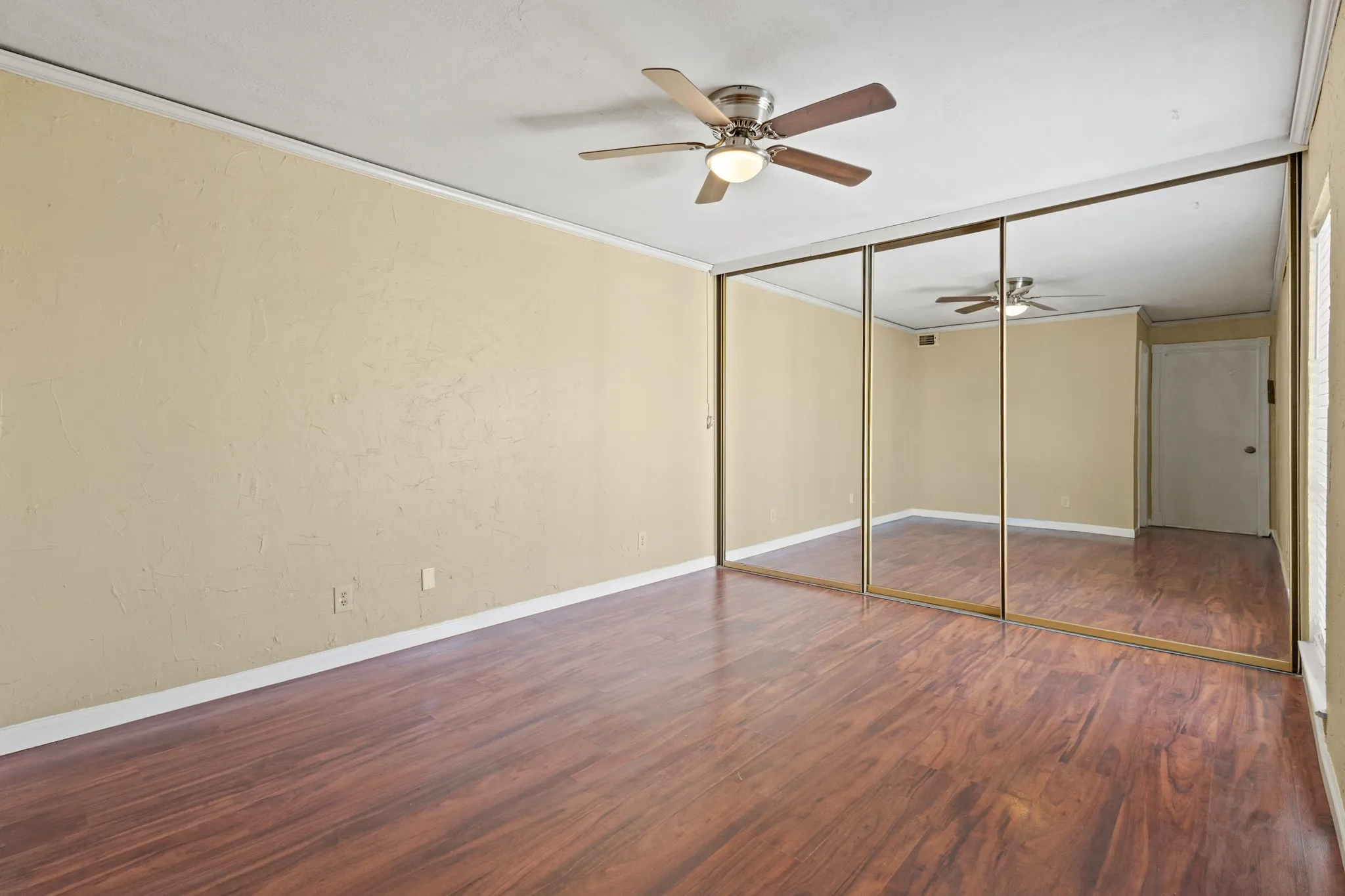 Unfurnished bedroom with wood finished floors, ornamental molding, a textured wall, a ceiling fan, and a closet