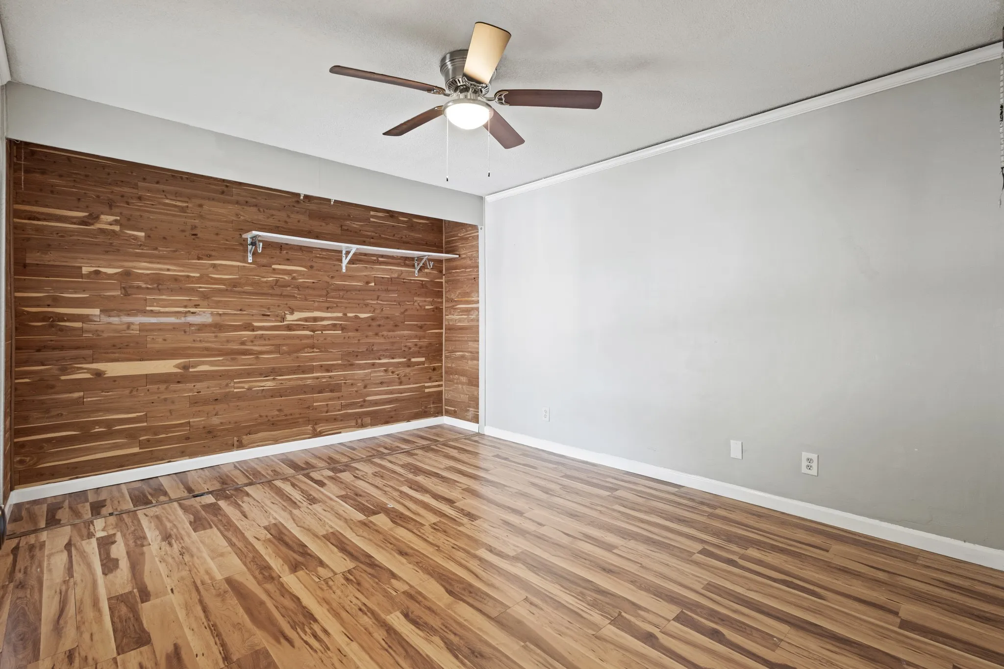 Unfurnished bedroom featuring wooden walls, wood finished floors, crown molding, and a ceiling fan