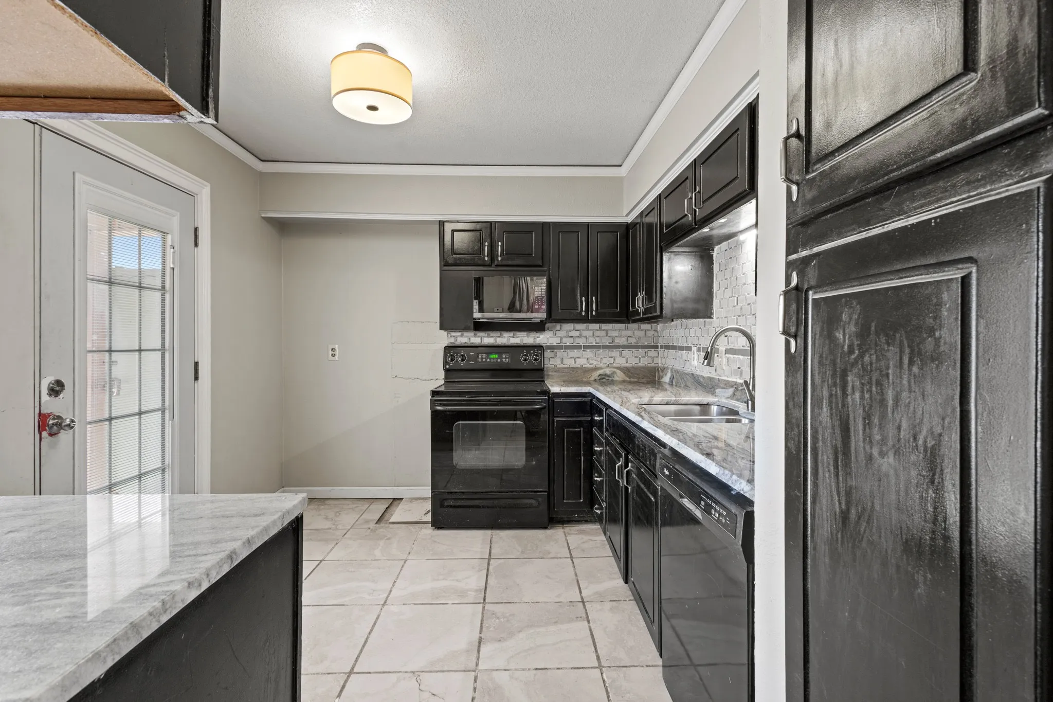 Kitchen with dark cabinetry, black appliances, light stone counters, backsplash, and ornamental molding