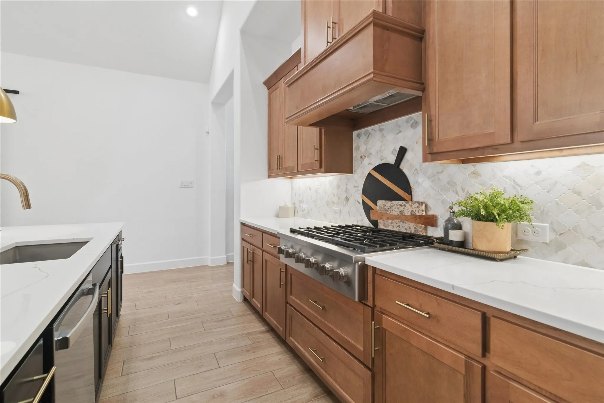 Gas cooktop with wood vented hood, white quartz countertops, marble tile backsplash.
