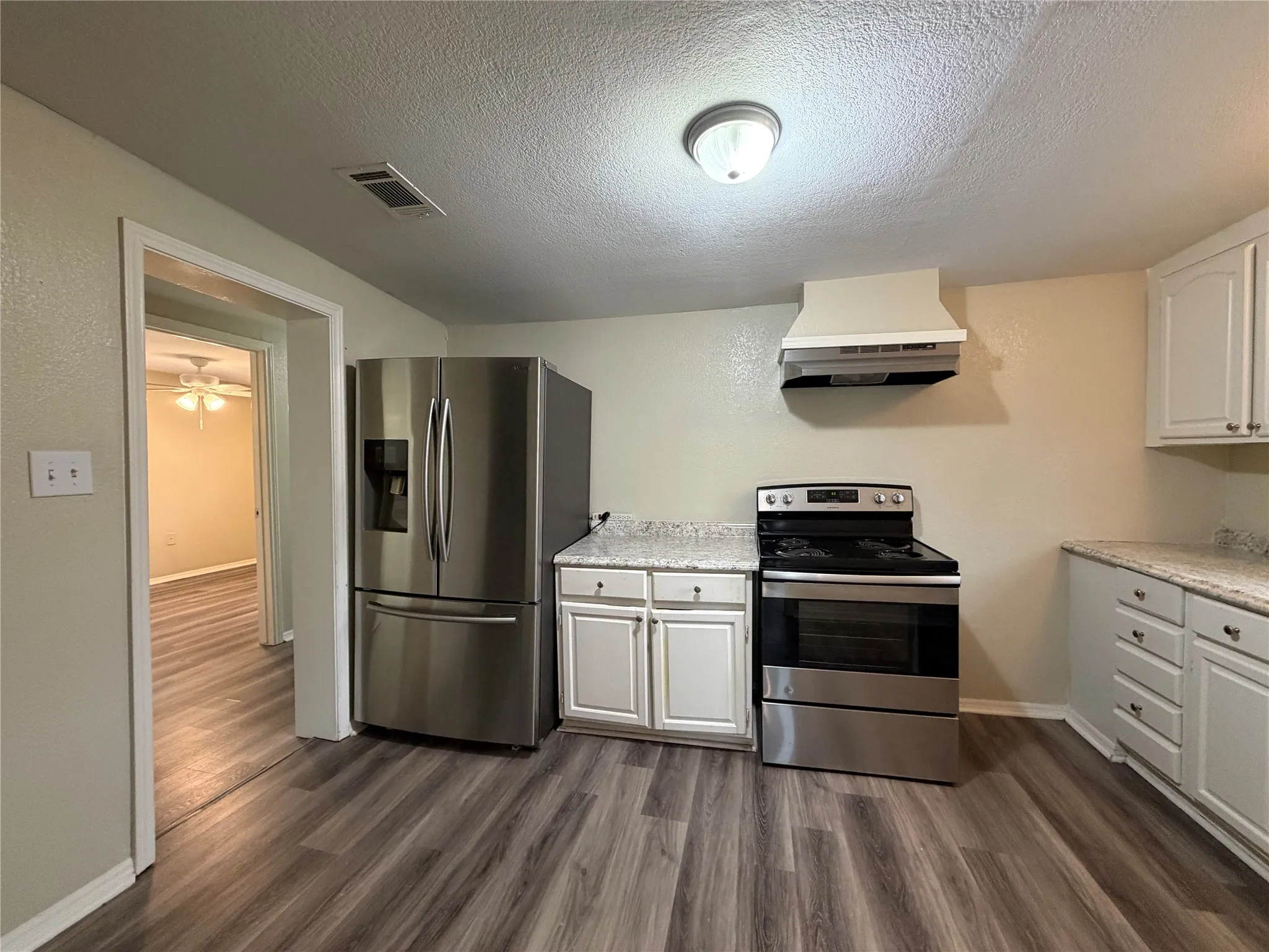 Kitchen with stainless steel appliances, white cabinets, a textured ceiling, dark wood-type flooring, and a ceiling fan