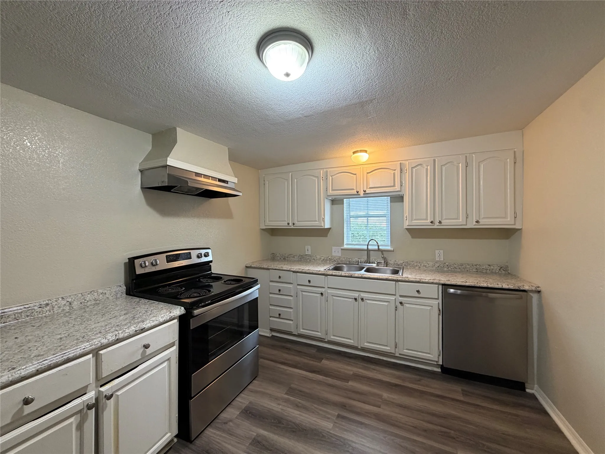 Kitchen with stainless steel appliances, white cabinets, a textured ceiling, and dark wood-style flooring