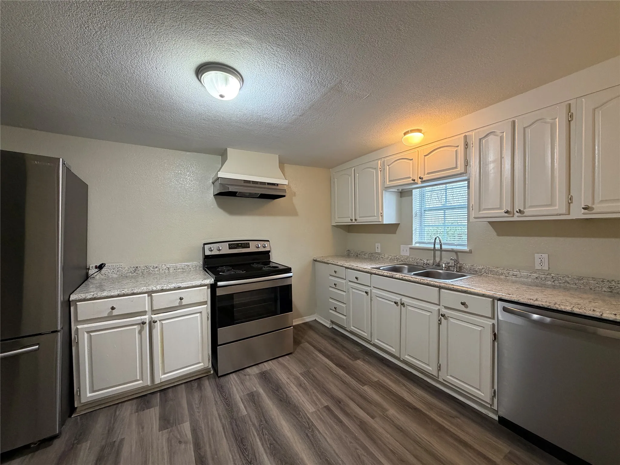 Kitchen featuring stainless steel appliances, white cabinetry, a textured ceiling, and dark wood finished floors