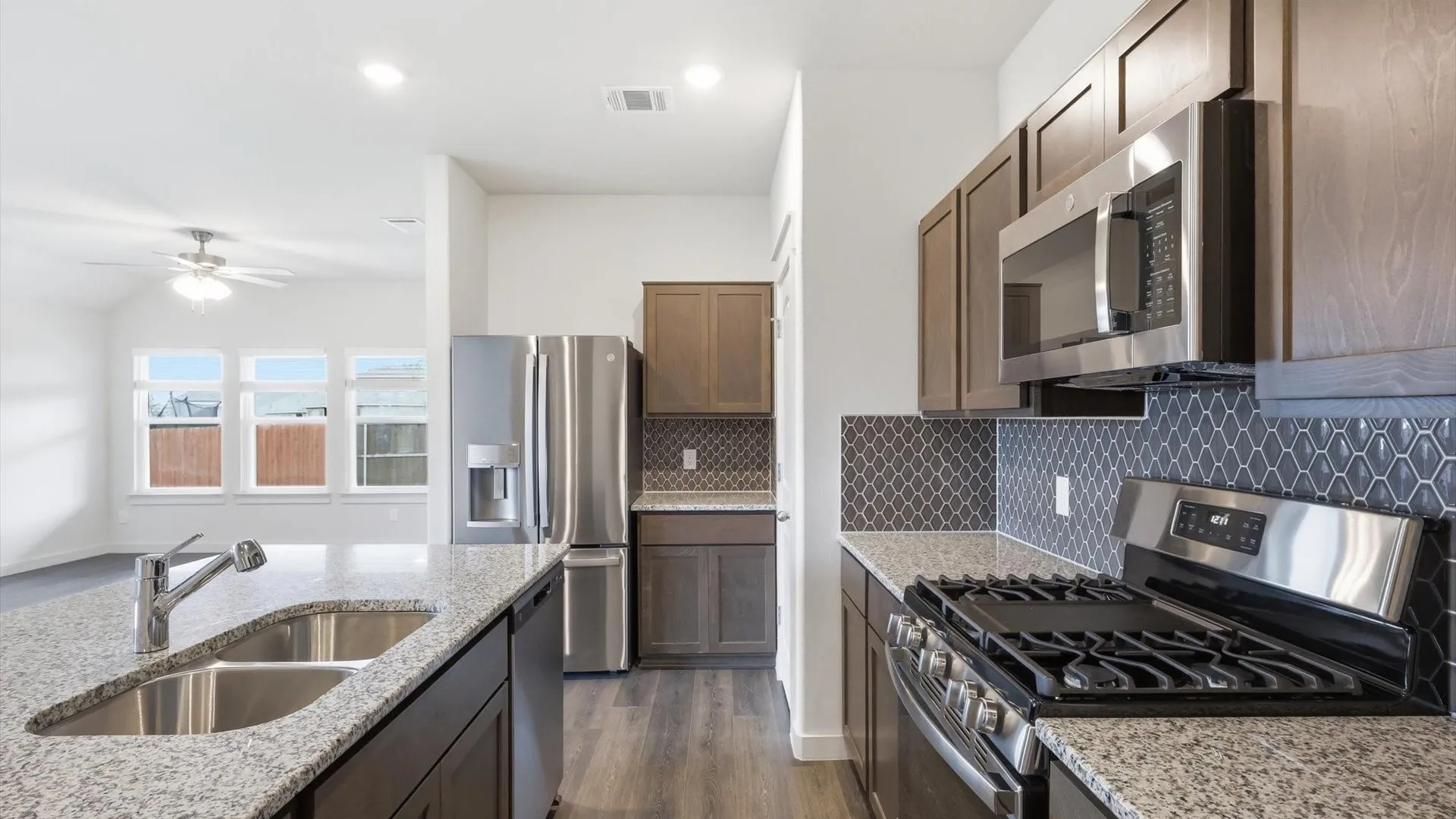 Modern kitchen featuring dark wood-finish cabinetry, stainless steel appliances, and light-toned granite countertops