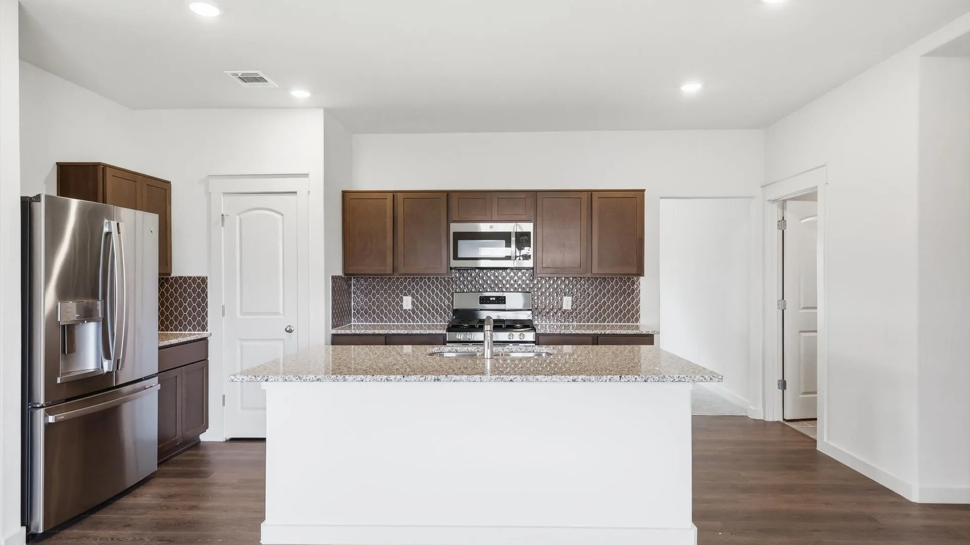 Kitchen featuring a center island with a double basin sink, stainless steel appliances, dark wood cabinetry, and patterned backsplash