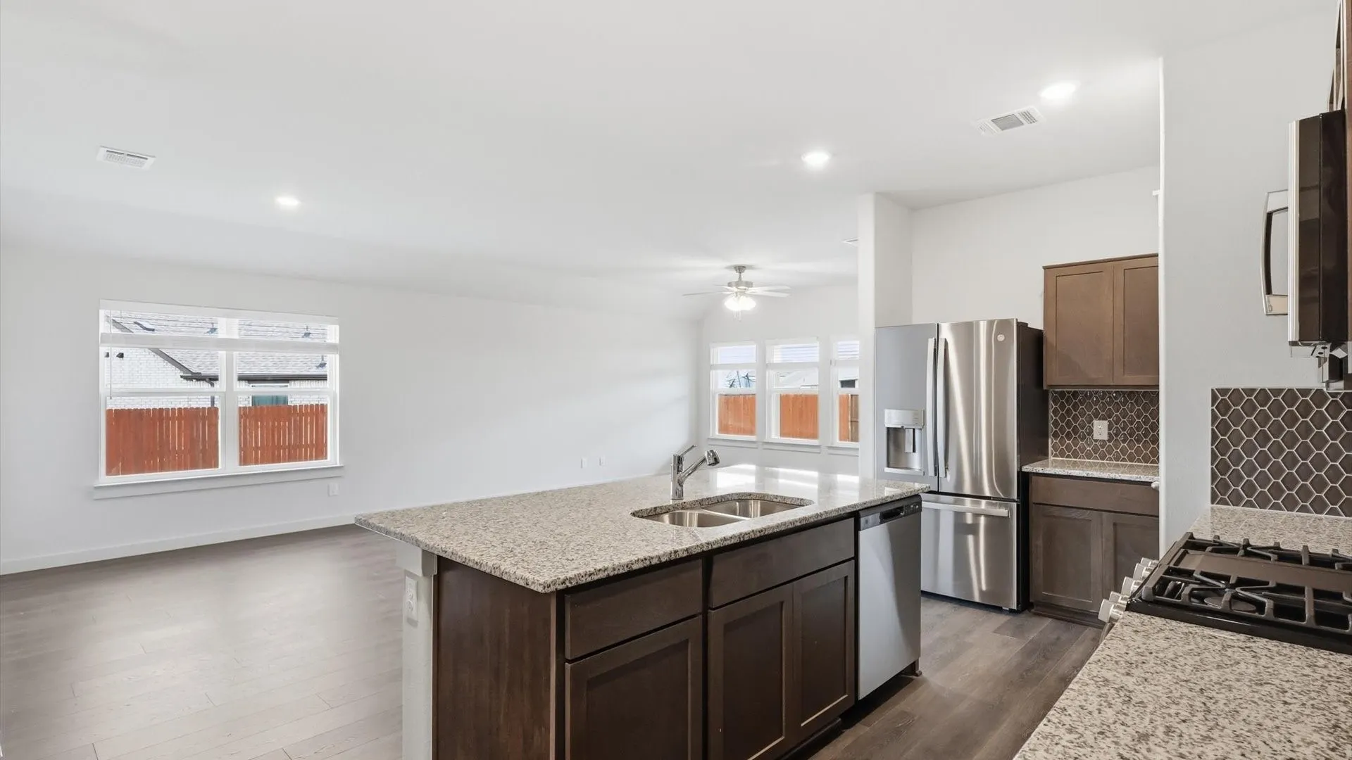 Open-concept kitchen featuring an island with a double basin sink, granite countertops, dark wood cabinetry, stainless steel appliances, and a mosaic tile backsplash