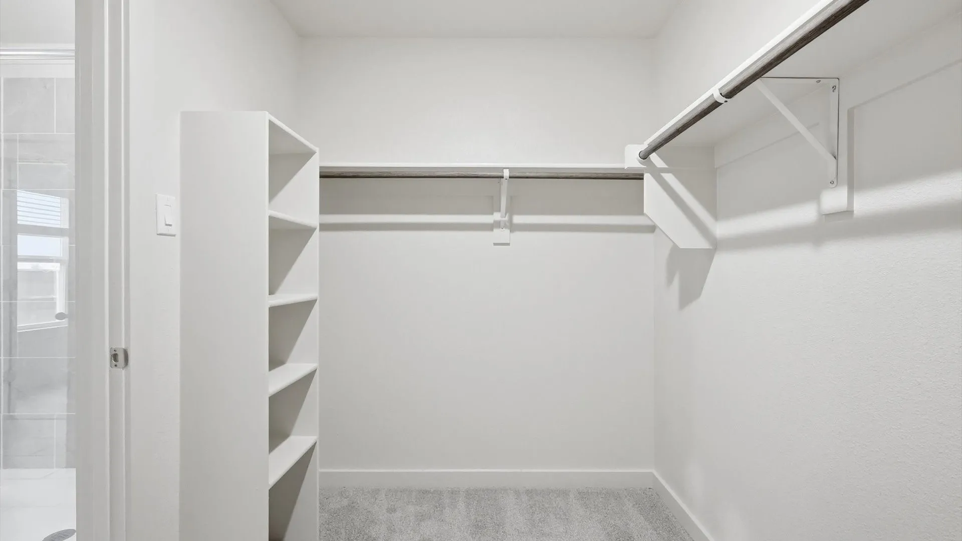 Walk-in closet featuring built-in shelving, two clothing rods, and light gray carpeting