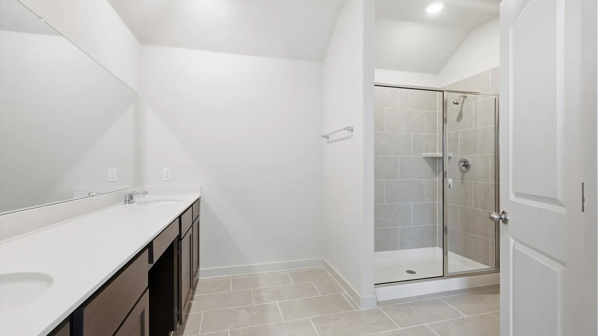 Bathroom featuring a dual vanity with white countertops, dark wood-finish cabinetry, and a full-width mirror