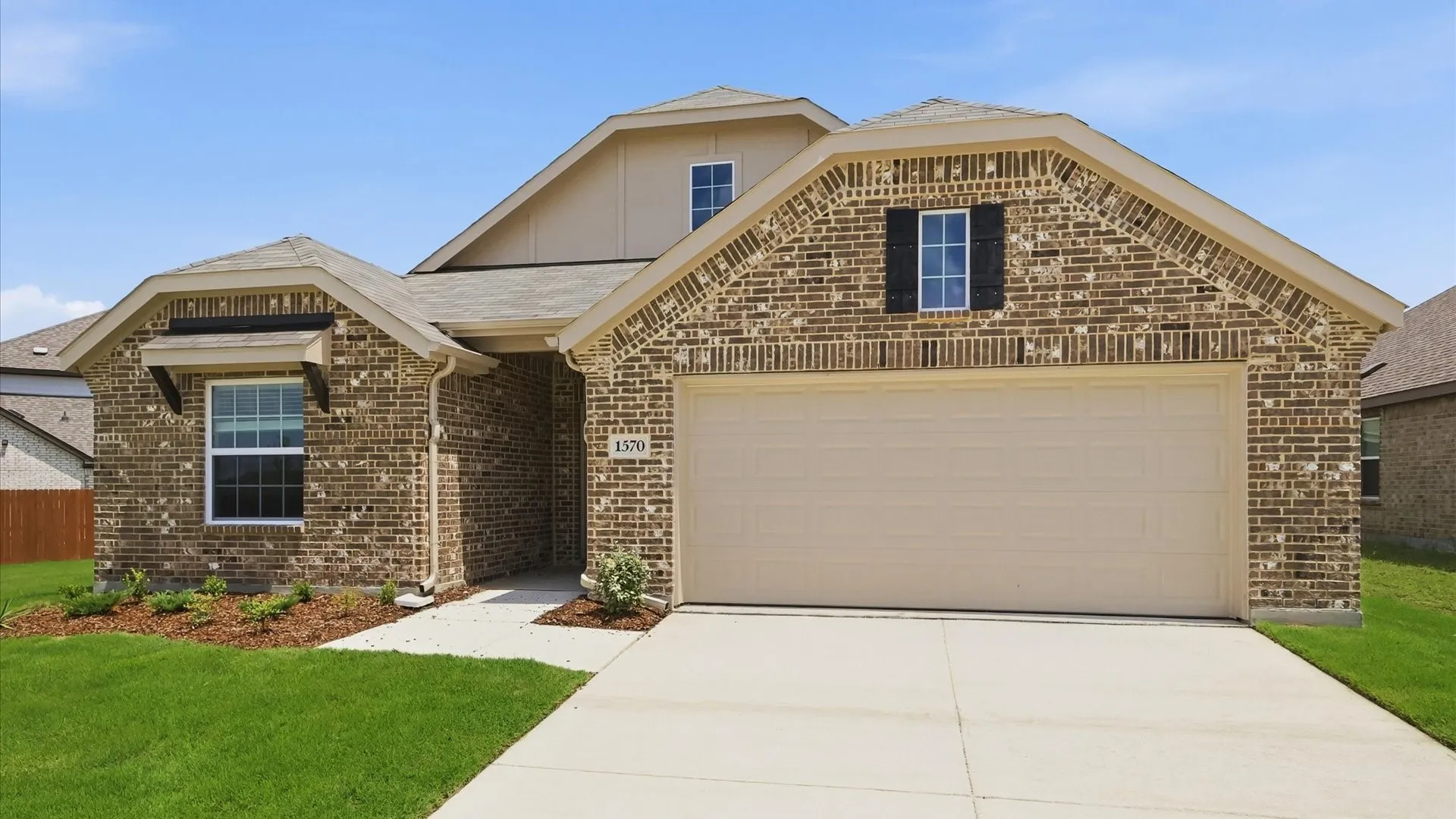 Brick exterior with a peaked roofline, an attached garage, a paved driveway, a concrete walkway, and a manicured lawn