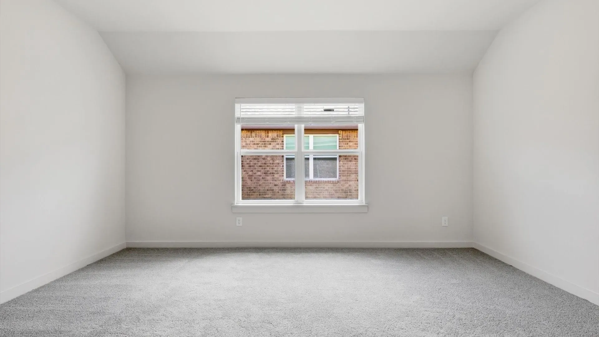 Bright interior space featuring a window with blinds, light gray carpeting, crisp white walls, and white baseboards