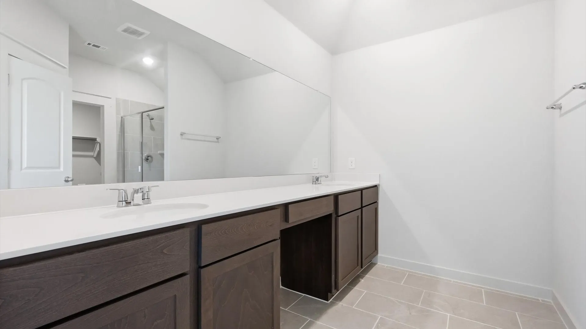 Bathroom featuring a long dual vanity with white countertops, dark wood-finish cabinetry, and chrome fixtures